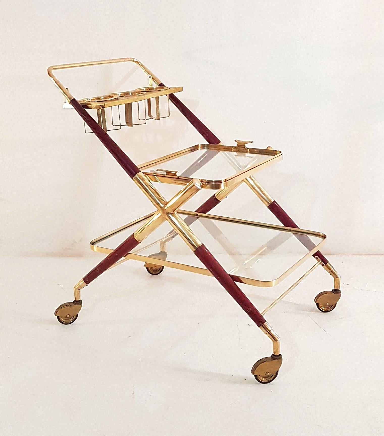 An all original midcentury bar cart by Cesare Lacca, Italy, in stained lacquered beech and brass with a design typical for Lacca. Two tiers with clear glass where the top tier doubles as a tray as well. And a holder for three bottles by the handle.