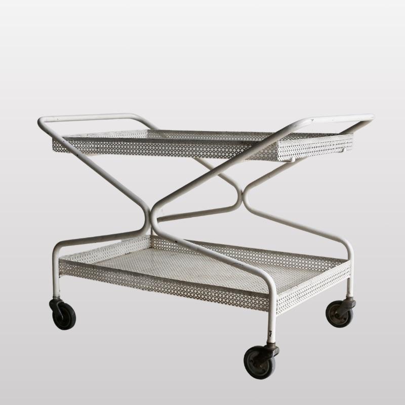 French work from the 1950s
Trolley” rolling table attributed to Mathieu Mategot
X-shaped tubular metal structure on four castors supporting two trays pierced in cloverleaf pattern and surrounded by fishnet.
Creamy-white lacquered metal