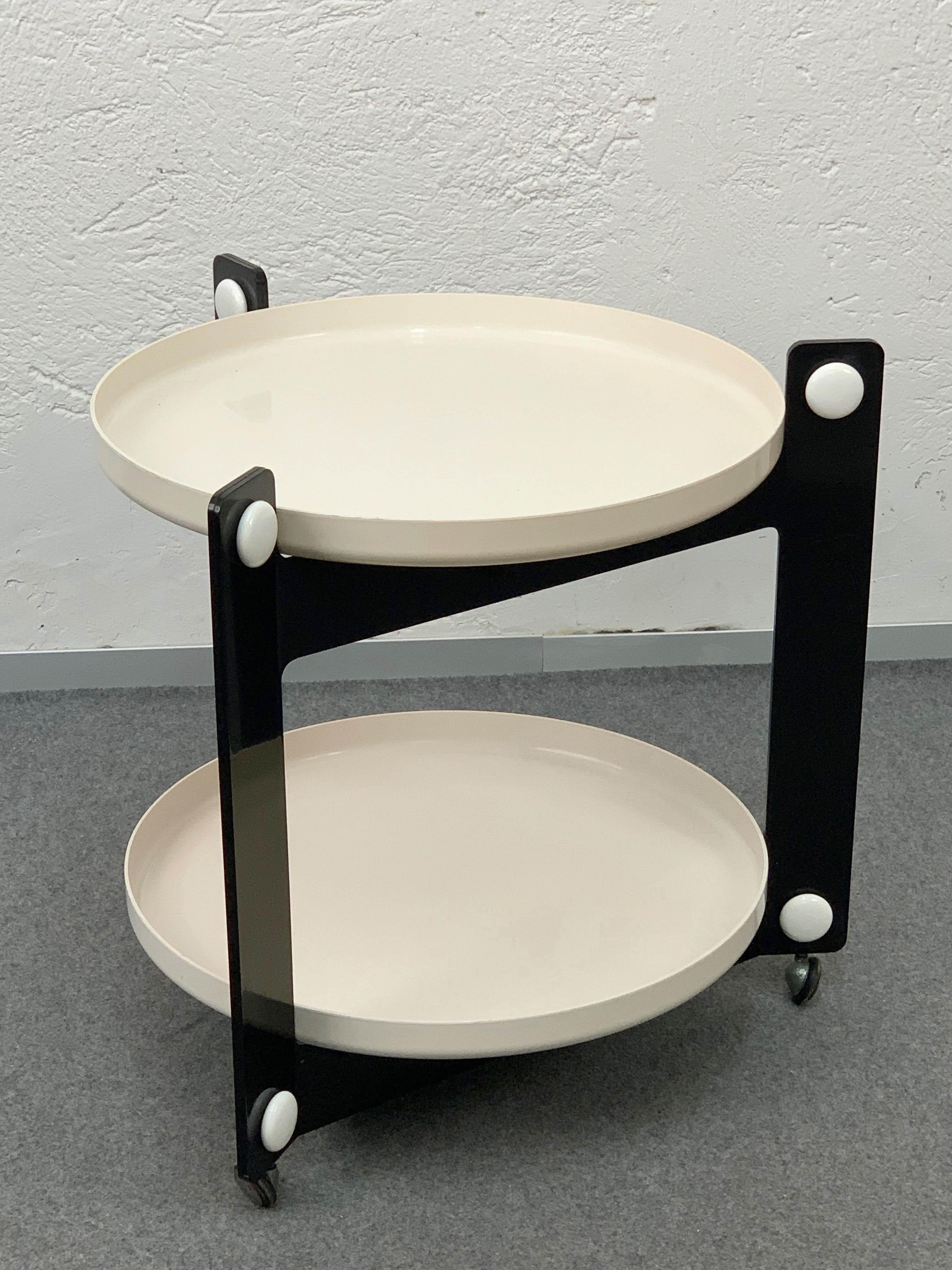 This Italian drinks trolley from the 1970s was designed by Luigi Massoni for Guzzini. 

The trolley has two trays, made of white plastic. These two removable circular shelves have a diameter of 56 centimetres and are located inside the completely