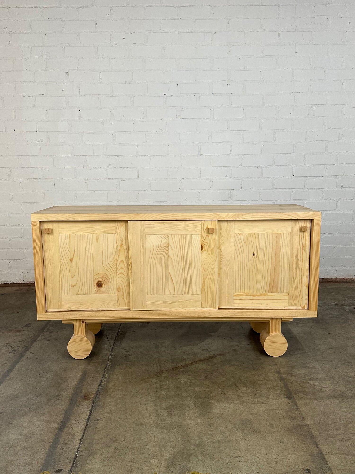 W60 D18 H32

Trolley Credenza made in house in solid Pine. Item has three sliding doors and two thick removable shelves. Credenza offers very nice dovetail corners and turned legs with a cross bar added for ample support. Hardware is also