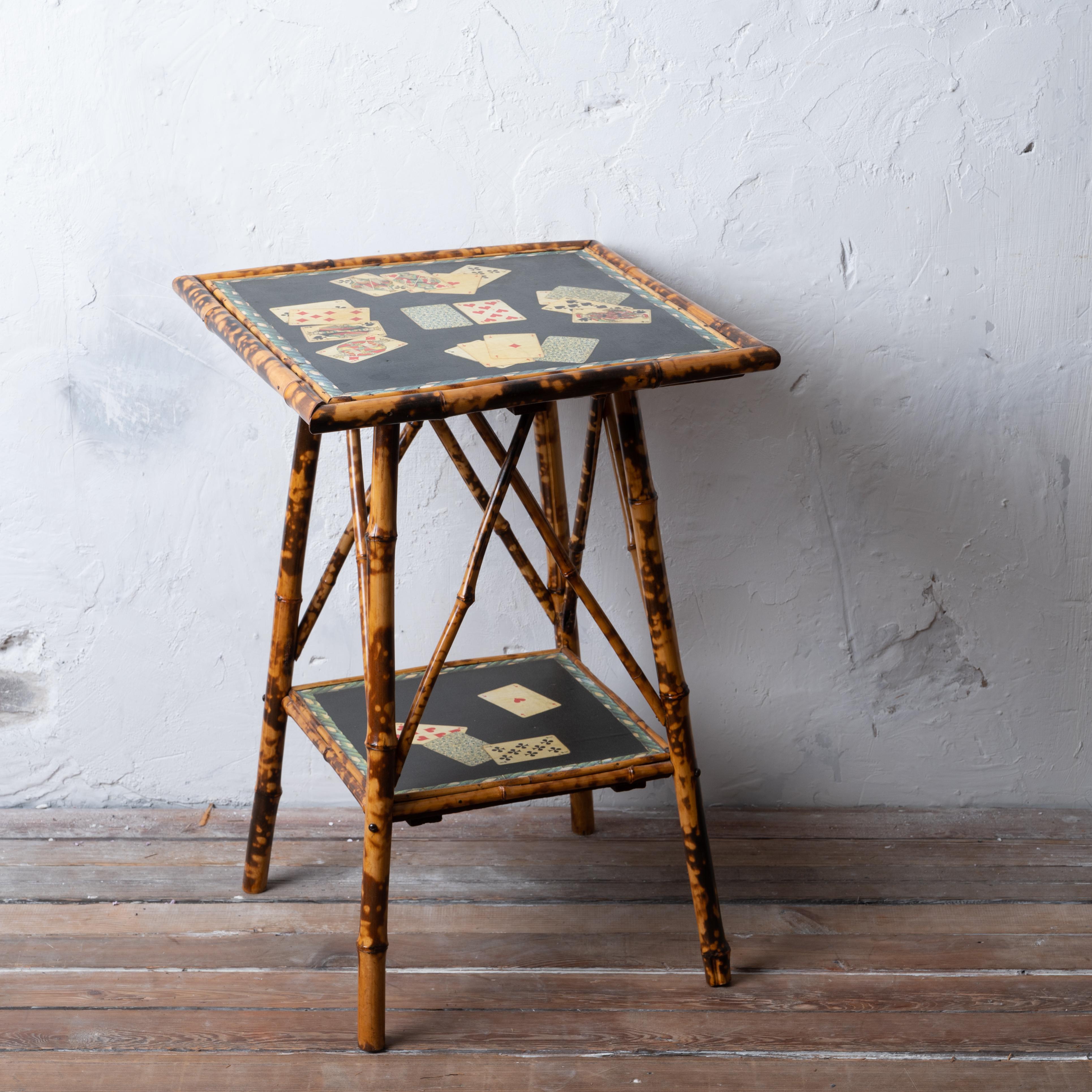 An English aesthetic period trompe l'oeil burnt bamboo two-tiered table with japanned top and decoupaged french playing cards, circa 1890s.

20 inches wide and deep by 29 inches tall


