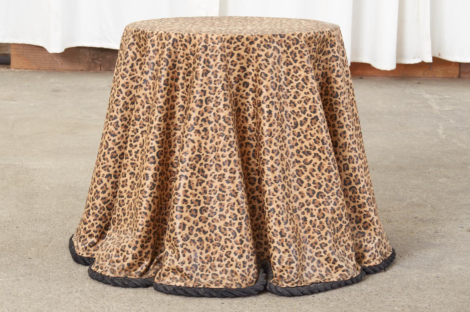 Fantastic Hollywood Regency drink table or side table featuring a trompe L'oeil draped fur cover. Handcrafted from fiberglass with a leopard, jaguar, or cheetah design and a black rope border. The fiberglass is draped over a round wood top and fans