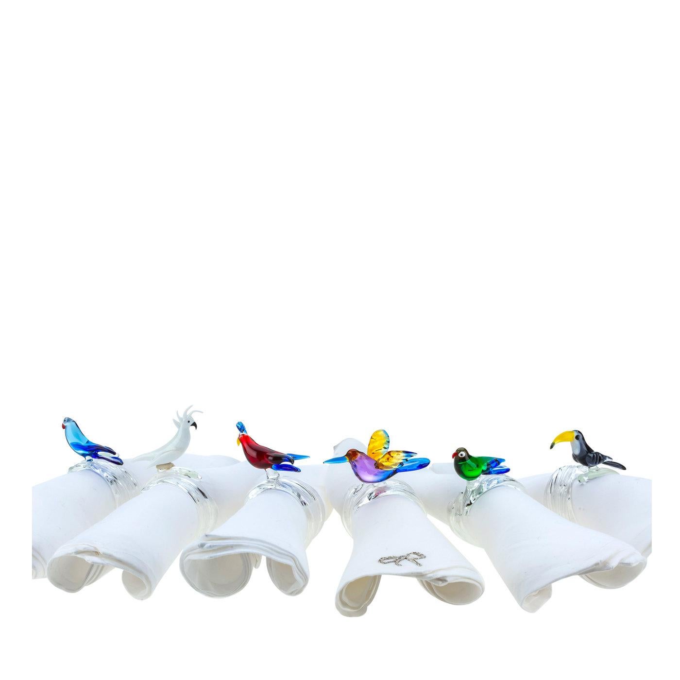 Functional and stylish, this set of six napkin rings boasts a skillful glass rendition of tropical birds in bright colors. A refined and charming addition to any table setting, this set includes a white cockatoo, a bird of paradise, a red bird, a