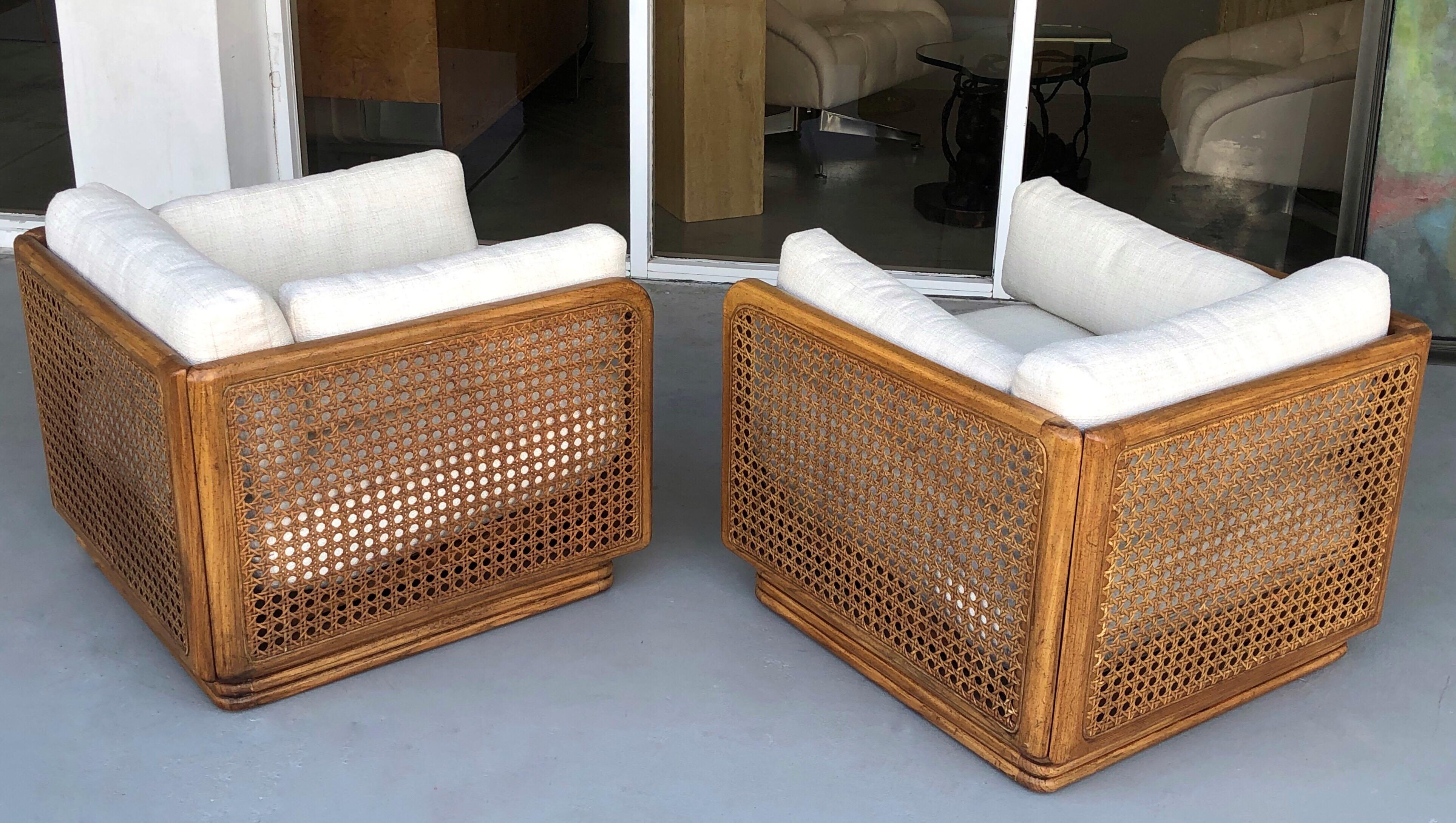 A pair of 1970s wood and cane swivel chairs. All removable cushions on an open square wood frame with large caning.