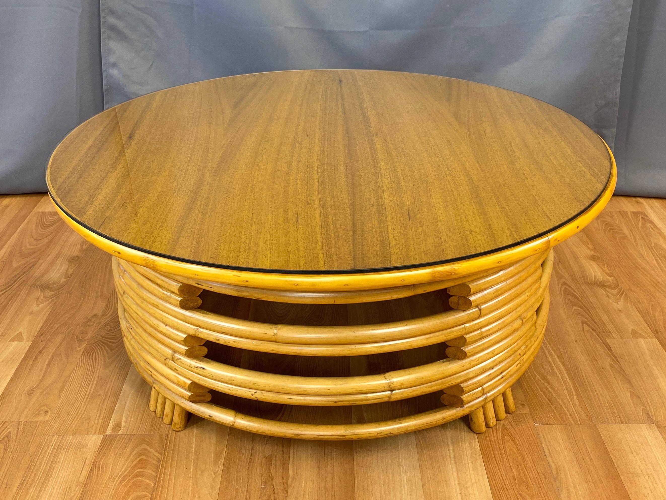 A very handsome mid-century Paul Frankl-style rattan and mahogany round coffee table by Tropical Sun Co. of Pasadena, California.

Expertly-crafted bent rattan stacked with alternating openings that give the curvaceous form a substantial yet open