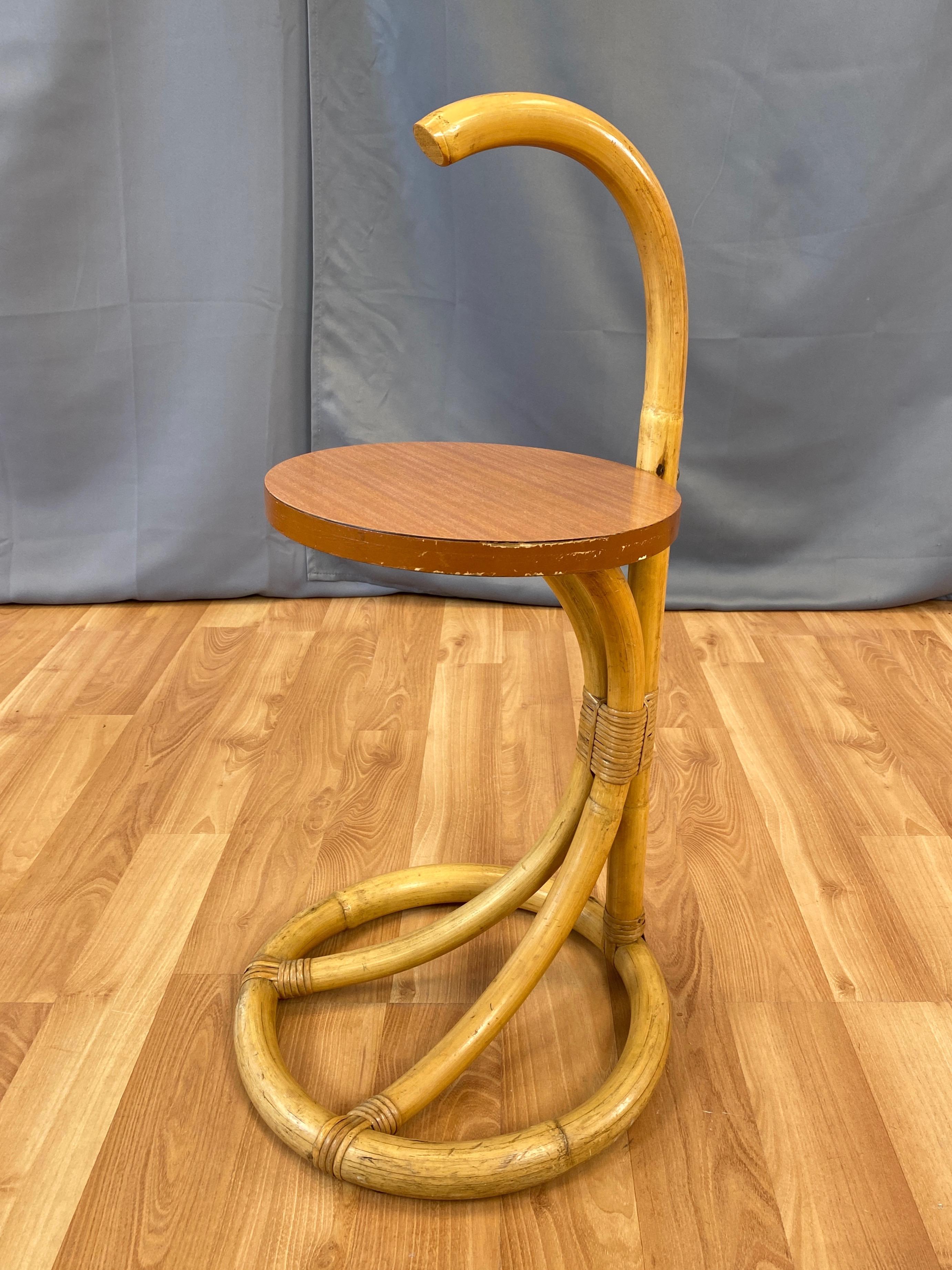 A charming little mid-century rattan and faux-mahogany cigarette, cocktail, or side table by Tropical Sun Co. of Pasadena, California.

Minimalist bent rattan design features a ring-shaped base, bowed supports, and a stem portion that resembles an