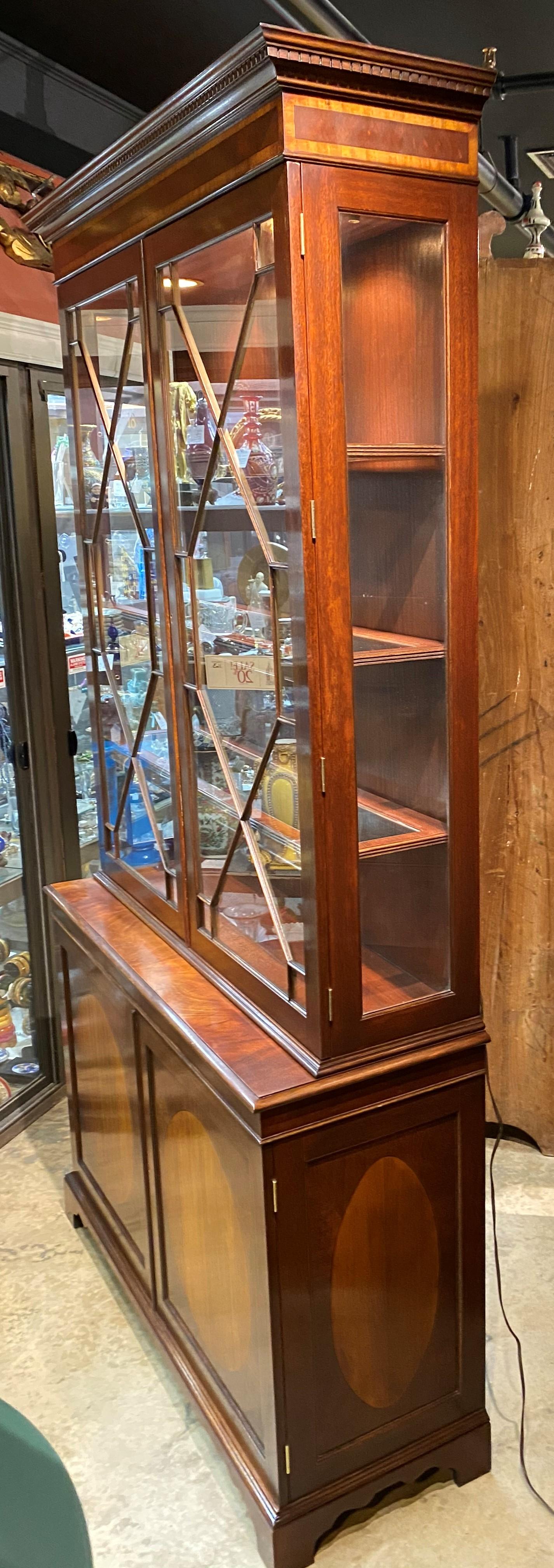 A fine Sussex Georgian style two part cabinet in mahogany and yew wood, its cornice with dentil molding, surmounting upper case with two glass doors, opening to a lighted interior with three adjustable glass shelves with wooden surrounds, and side