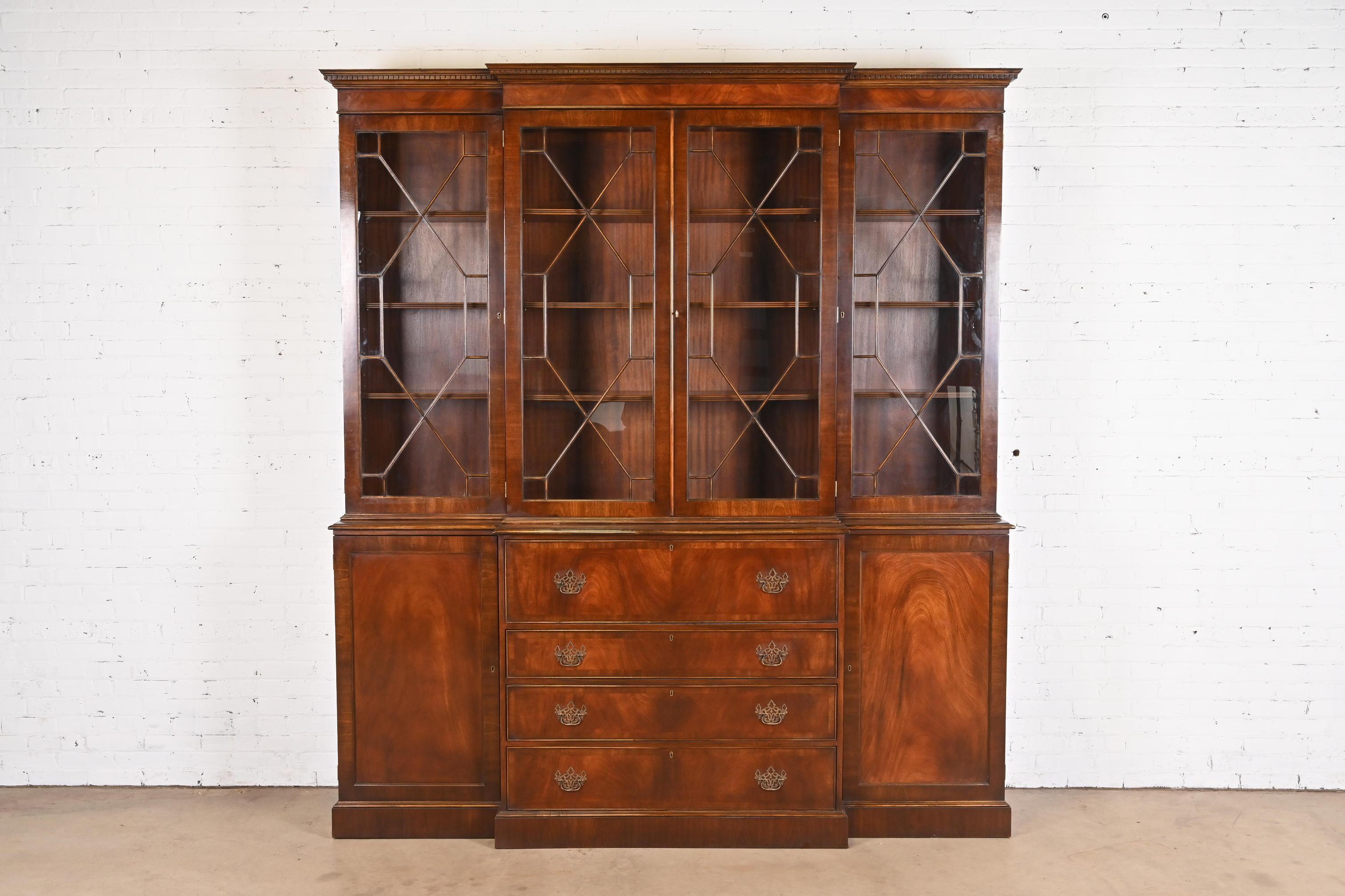 A gorgeous Georgian or Chippendale style monumental breakfront bookcase cabinet with drop front leather top secretary desk

By Trosby Furniture

USA, Circa 1980s

Carved flame mahogany, with mullioned glass front doors, original brass hardware, and