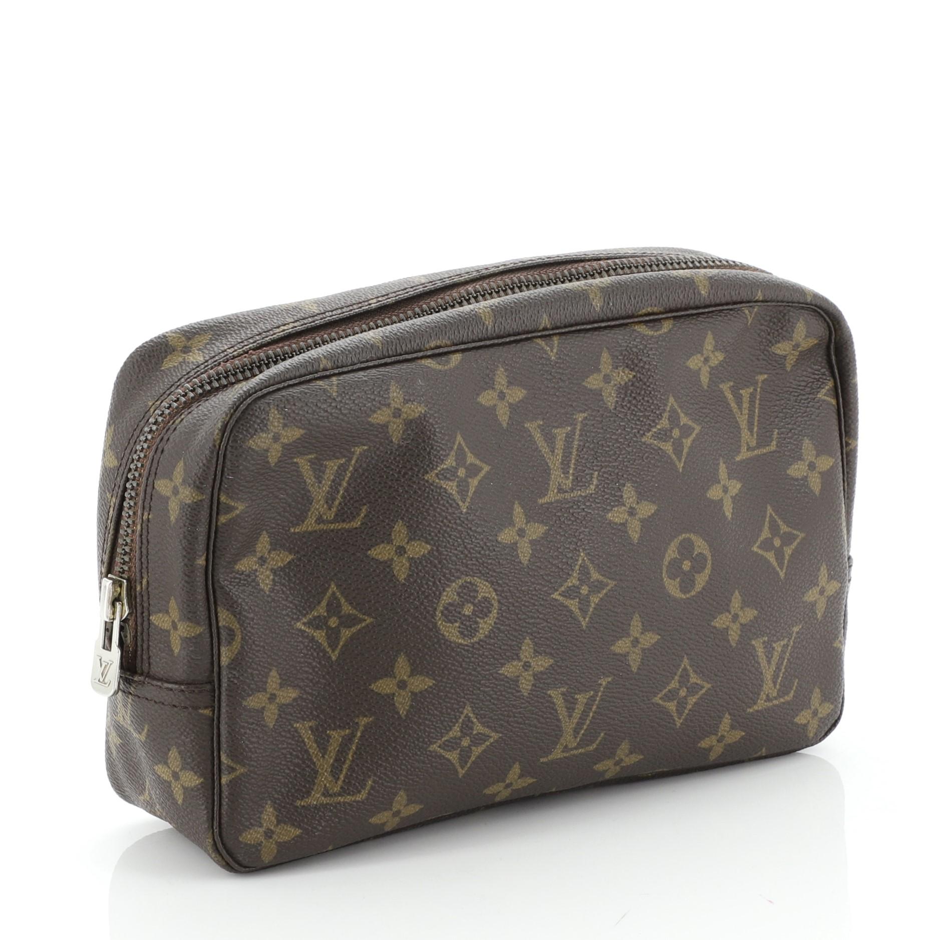 This Louis Vuitton Trousse Toiletry Pouch Monogram Canvas 23, crafted in brown monogram coated canvas, features gold-tone hardware. Its zip closure opens to a neutral leather interior. 

Condition: Damaged. Missing code. Wear and creasing on