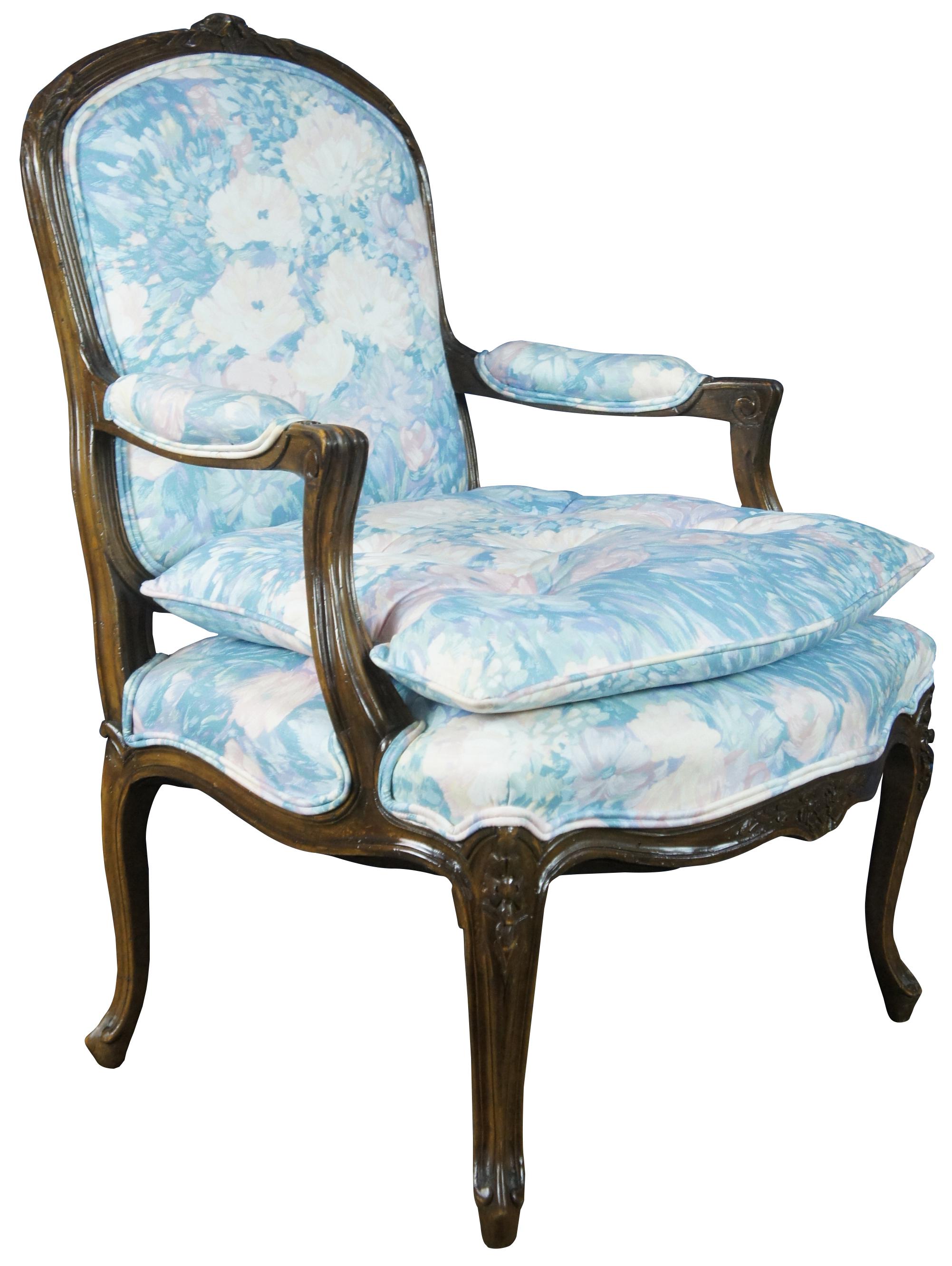 Vintage French Louis XVI style walut fauteuil serpentine armchair by Trouvailles Inc of Watertown, Ma. Made of walnut featuring serpentine form with padded arms, cabriole legs and carved floral and fluted accents. Upholstered in a floral Monet /
