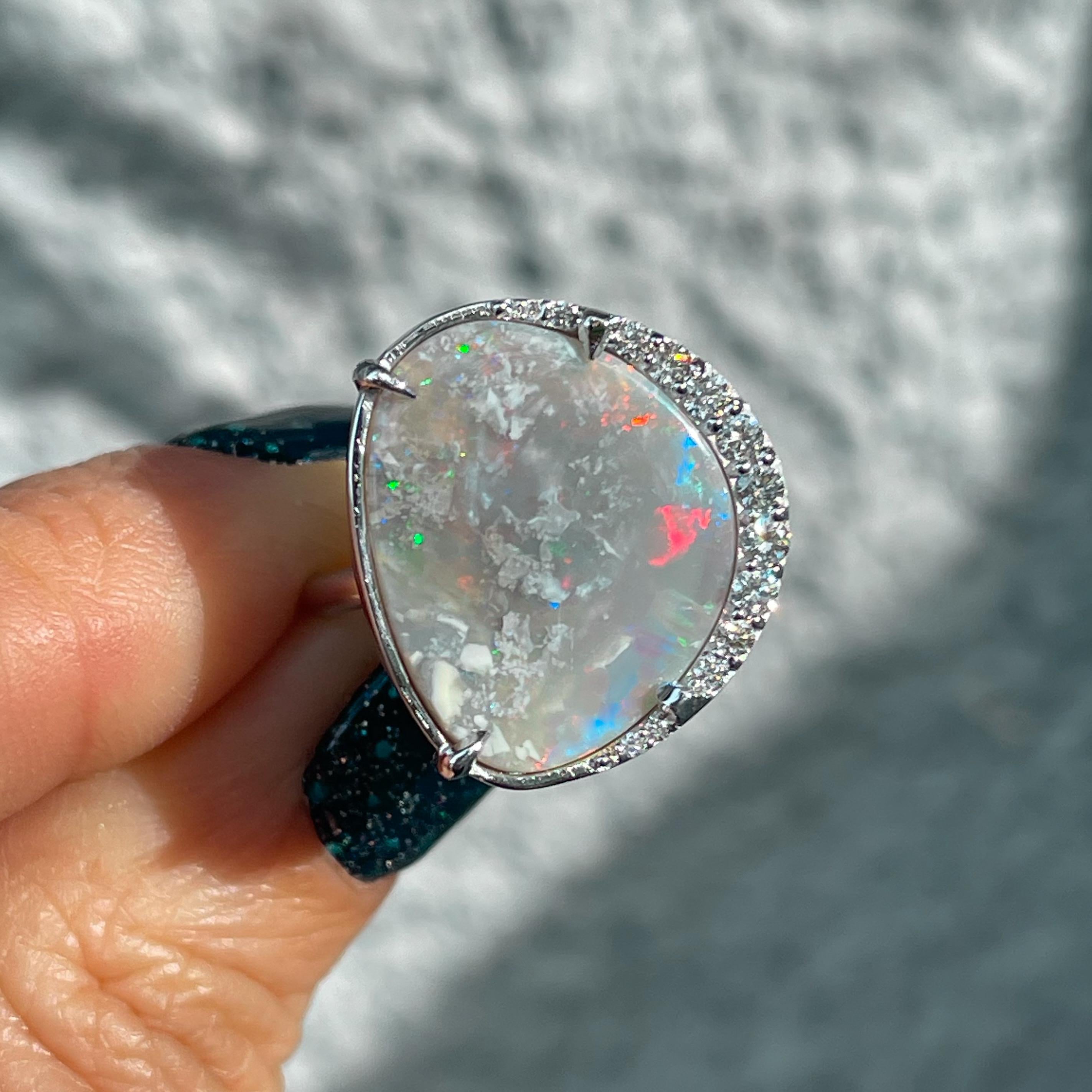 A myriad of color emerges through veiled grey in this Australian Opal Ring. Set in 14k white gold, the opal and diamond ring tenders a stark canvas. Against its white gold mounting, the colors within the Semi Black Opal spark with distinction. A