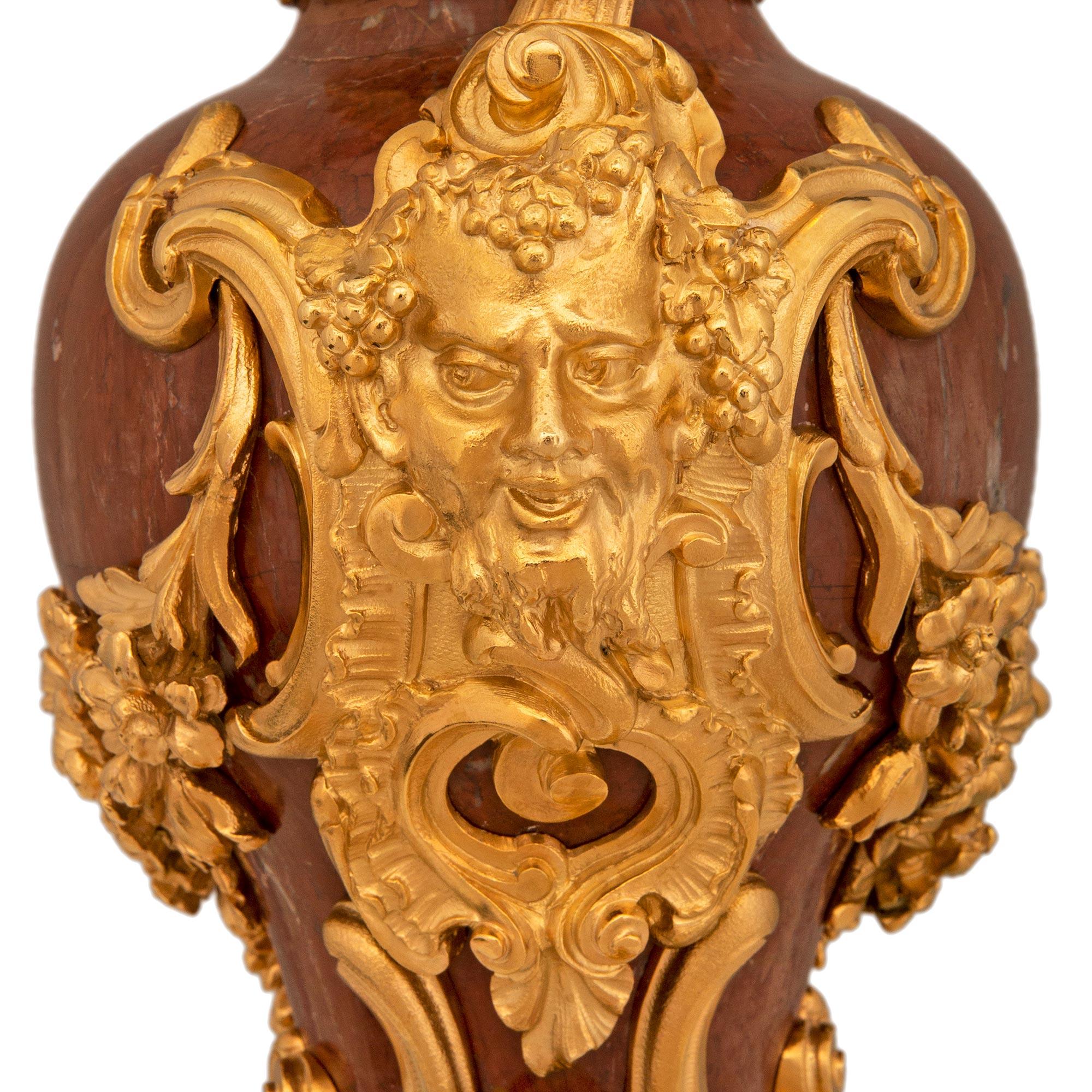 Une superbe paire de lampes en bronze doré et rosso Antico du 19ème siècle, de style Louis XV. Rosso Antico et Ormolu. Chaque urne asymétrique montée en lampe est surmontée d'une base en bronze doré percée, ornée de feuilles d'acanthe enroulées et