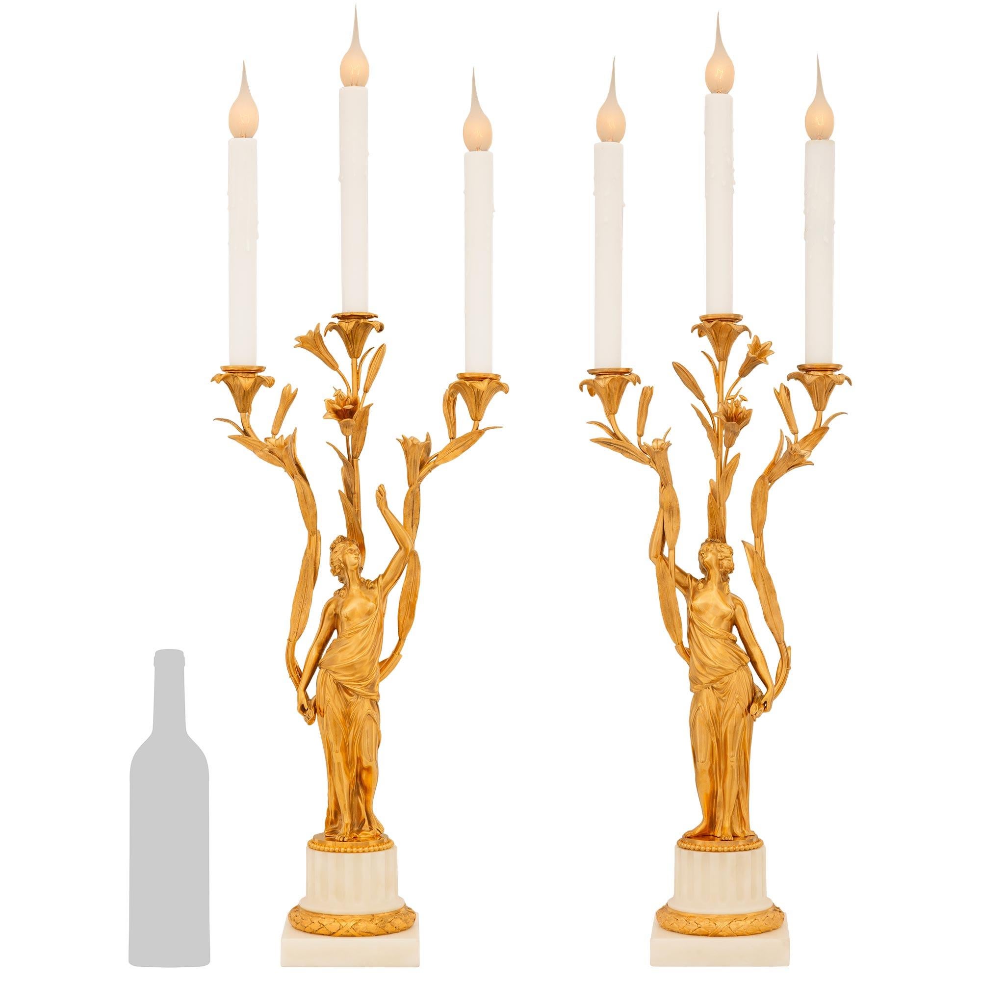 Un'attraente ed elegante coppia di lampade a candelabro francesi del XIX secolo in stile Luigi XVI in ormolu e marmo bianco di Carrara. Ogni splendido candelabro a tre bracci poggia su una base circolare scanalata in marmo bianco di Carrara,