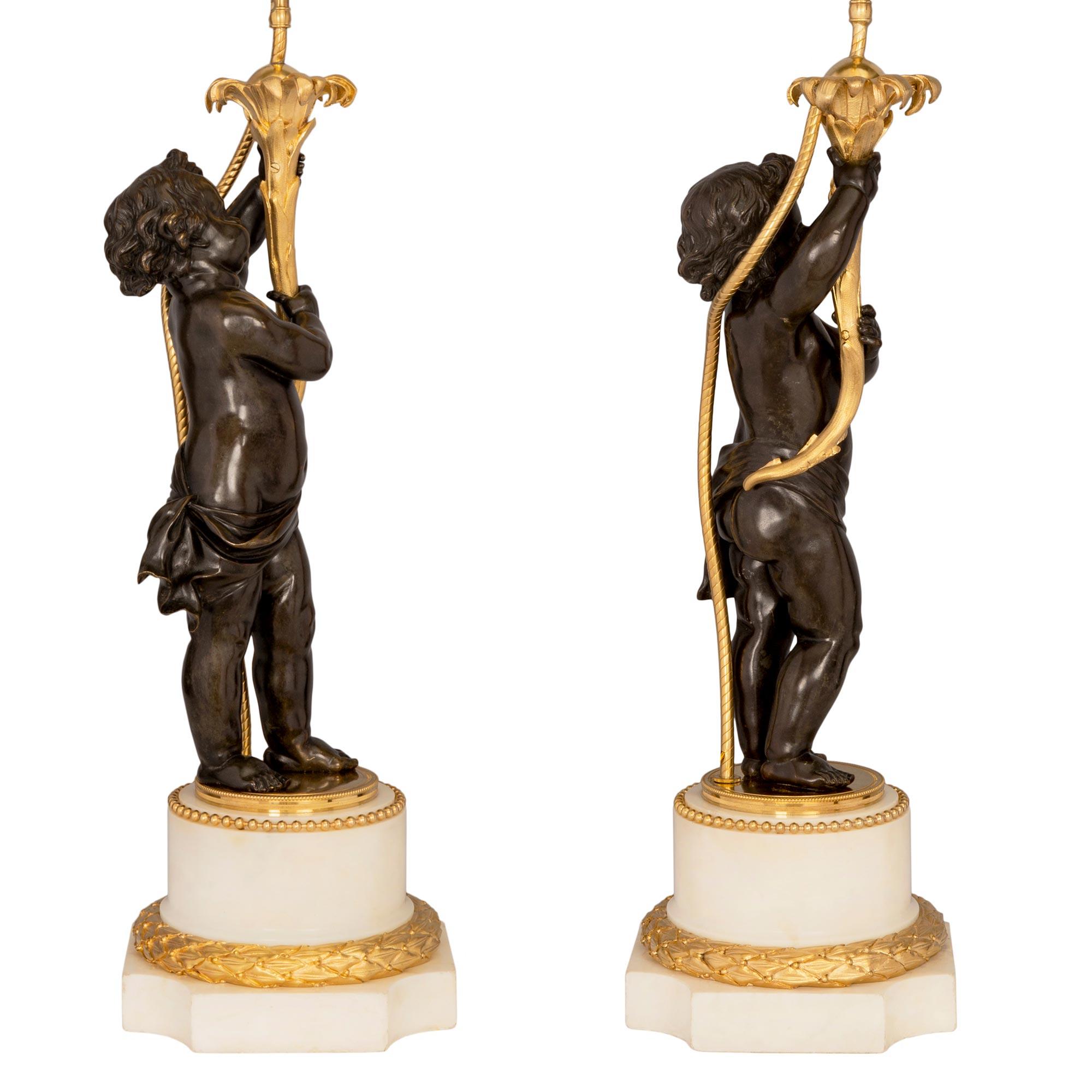 A most elegant and high quality true pair of French 19th century Louis XVI style patinated bronze, ormolu and white Carrara marble lamps. Each lamp is raised by a square base with concave corners and a striking berried laurel wraparound ormolu band.
