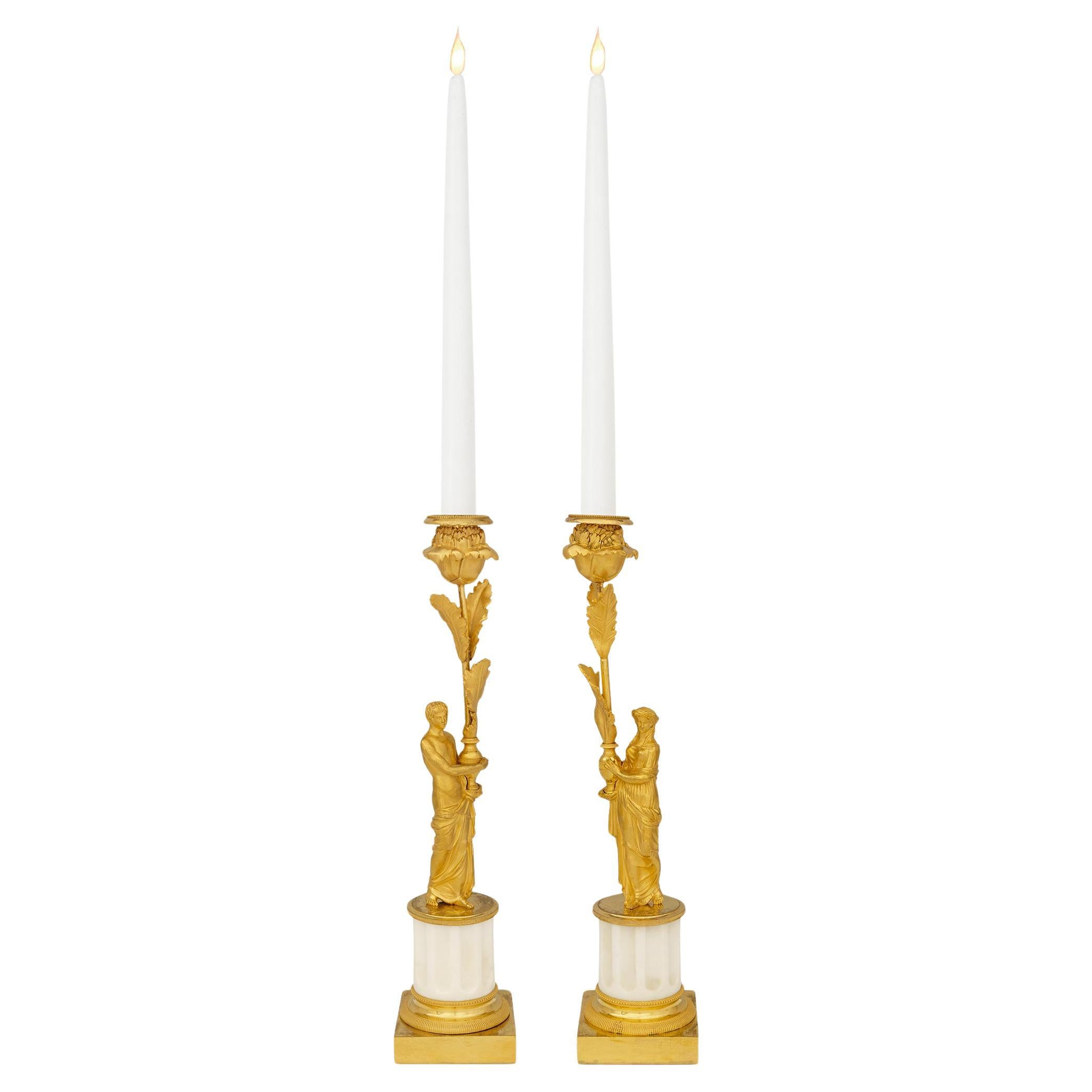 A striking true pair of French 19th century Louis XVI st. Ormolu and white Carrara marble candlesticks. Each richly detailed candlestick is raised by a square Ormolu base and socle displaying finely reeded wrap around bands. The circular fluted