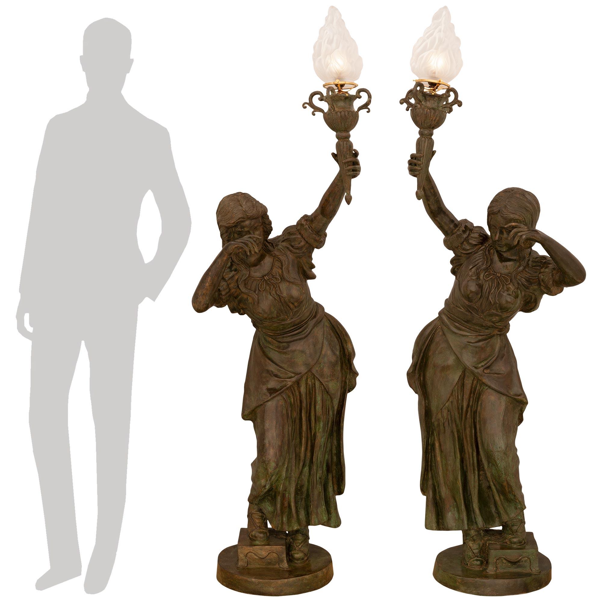 Una coppia di statue Torchière in bronzo Verdigris di fine secolo, squisita e finemente dettagliata. Ogni attraente statua/lampada da terra mostra una bella fanciulla vestita con abiti fluenti, sostenuta da una base circolare sotto un piedistallo