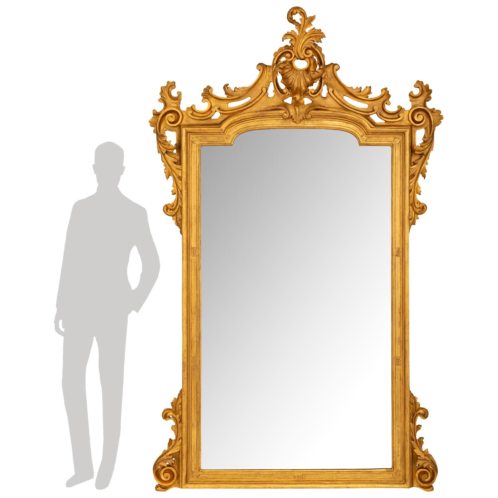 Magnifique paire de miroirs en bois doré de style Louis XV italien du XIXe siècle, finement détaillés. Chaque miroir repose sur des pieds à volutes flanquant le cadre finement détaillé aux bords marbrés et aux réserves de rosettes sculptées menant à