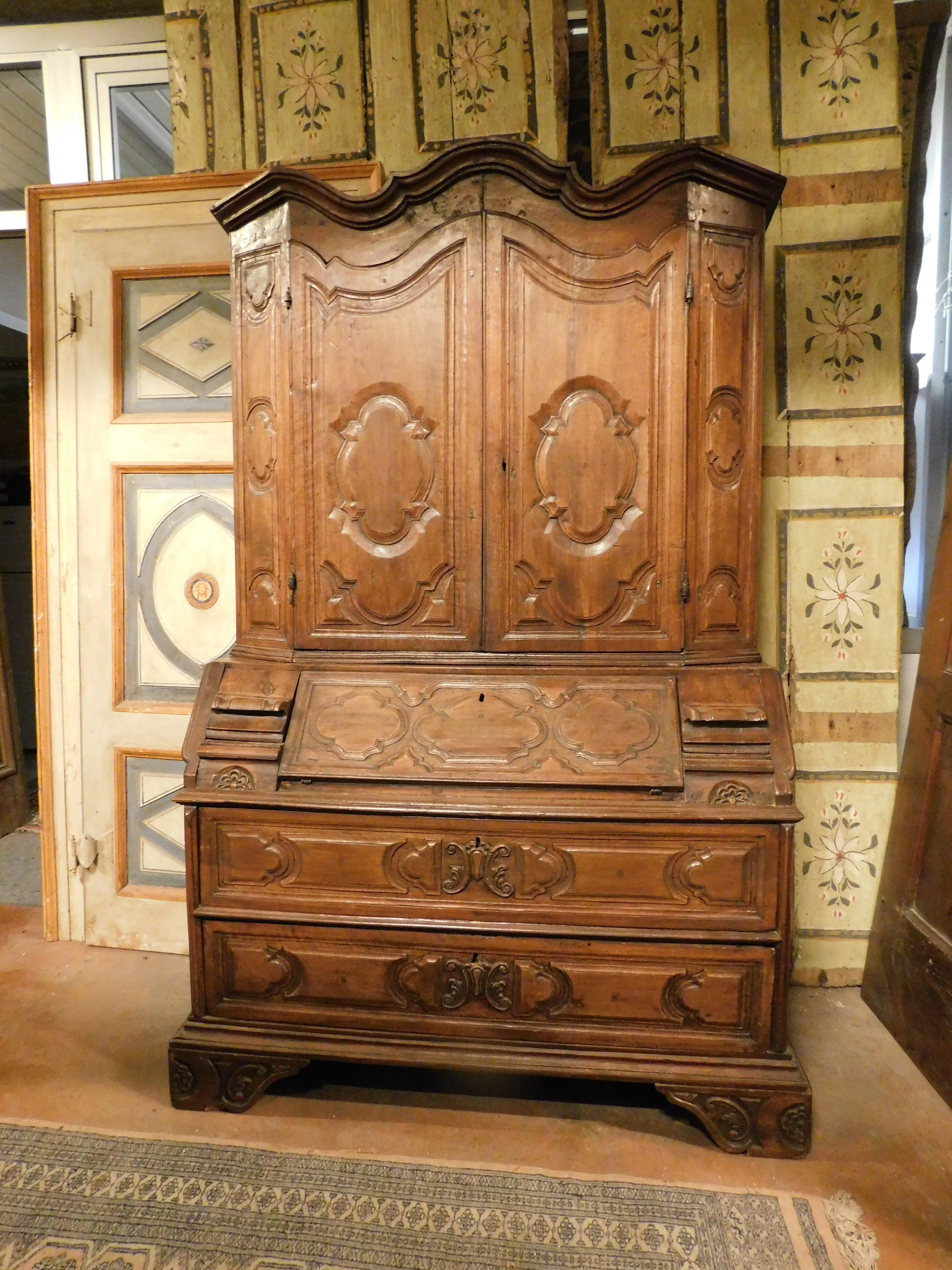 Antique Trumeau, piece of furniture in solid walnut, hand-carved with geometric and floral shapes typical of the late Baroque, upper part composed of two doors with shelves and base of two drawers and folding top that conceals three drawers, has
