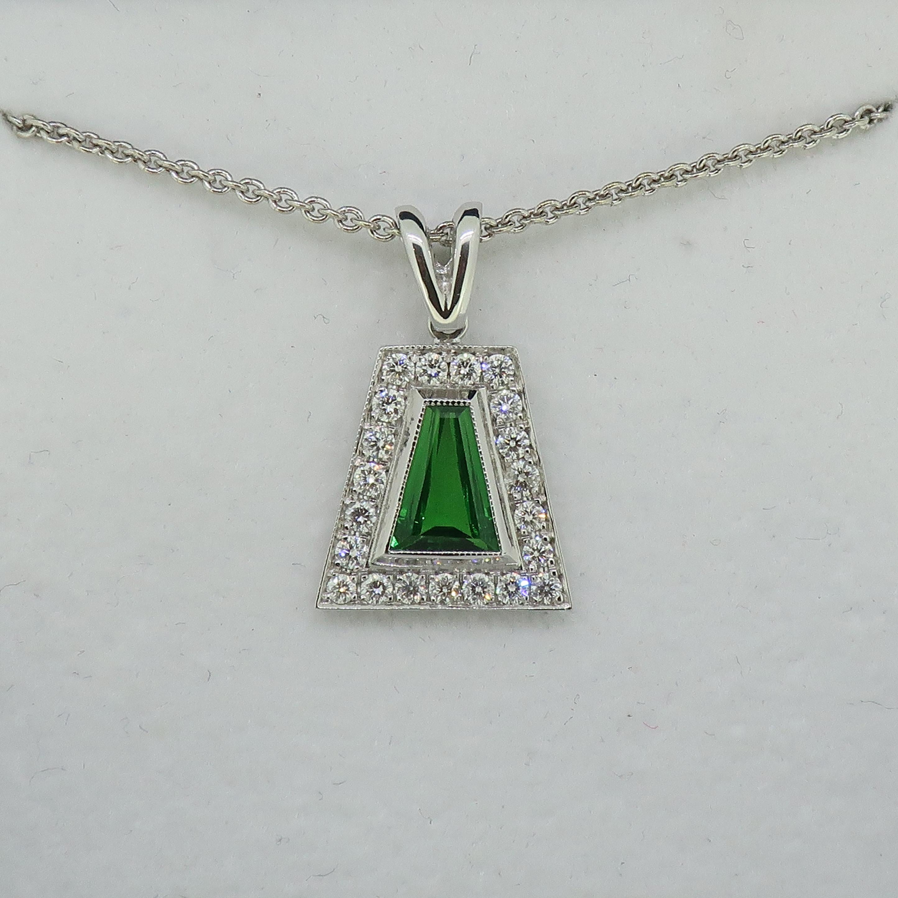 Tsavorite and Diamond Pendant 18 Karat White Gold 

Unusual tsavorite and diamond pendant. Bright green tsavorite in an tapered baguette shape, surrounded by twenty-one white brilliant cut diamonds. All stones set in a fine mill-grain setting,