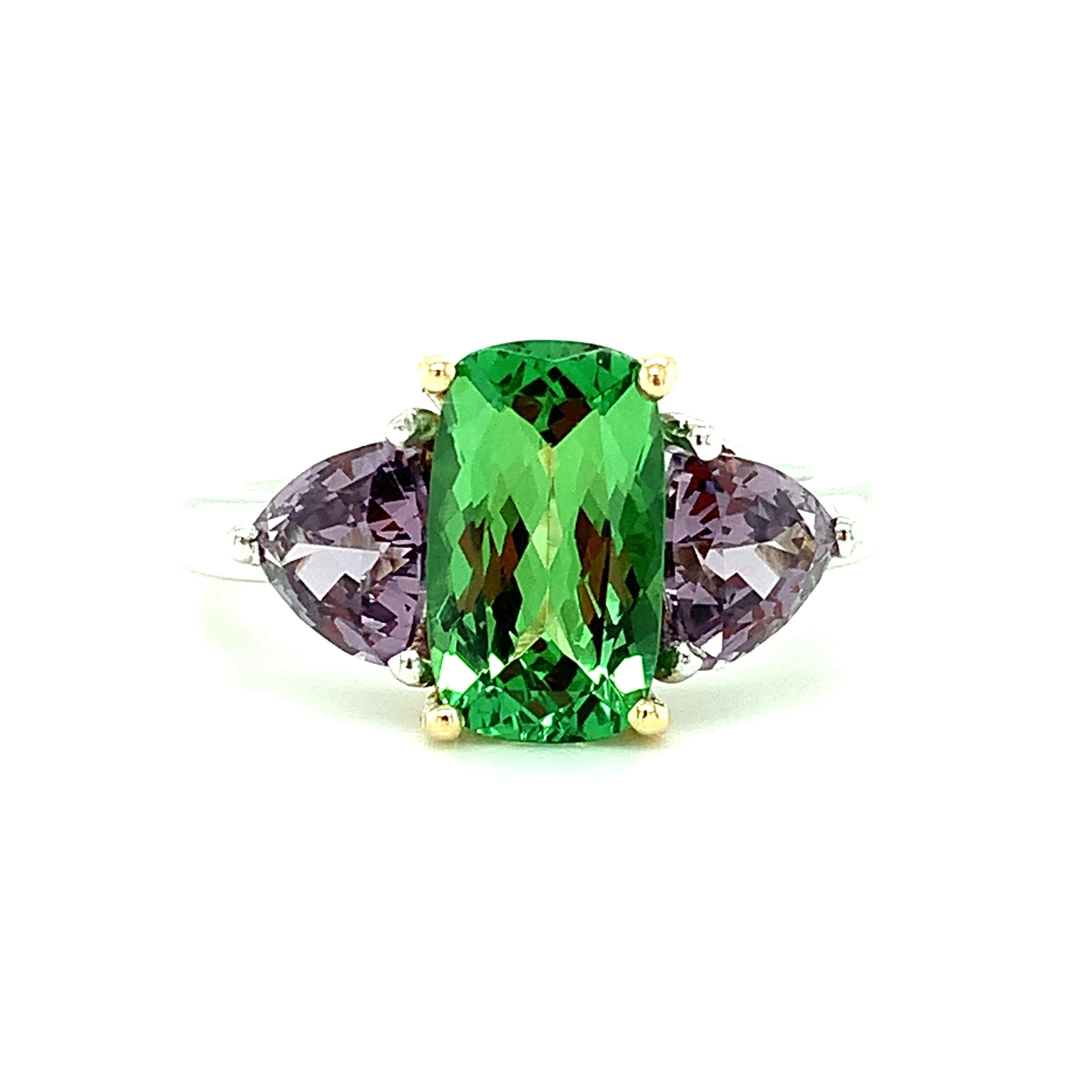 If you love rare and beautiful gemstones, this stunning ring is perfect! We have paired a bright green, 2.12 carat Tsavorite garnet with trilliant-cut purple spinels in one of nature's favorite color combinations! The tsavorite is a brilliant