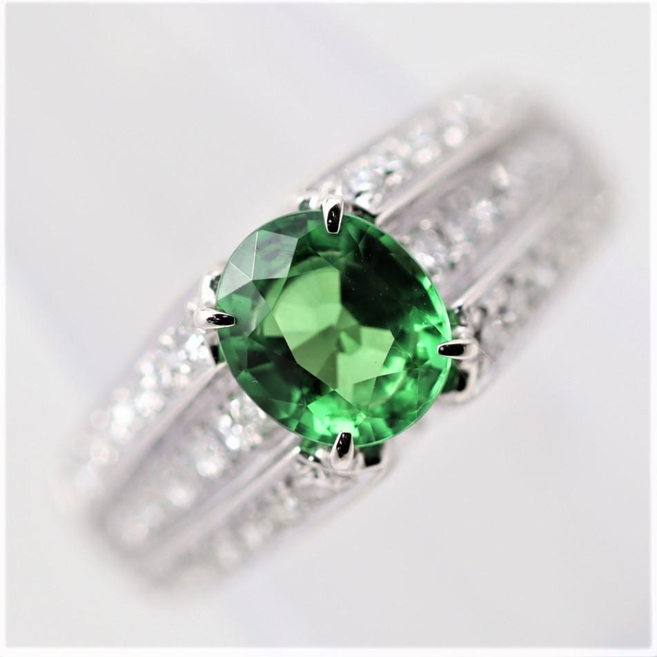 A fantastic ring featuring a fine tsavorite garnet weighing 1.95 carats. It has a lovely oval-shape along with strong rich grass-green color. It is complemented by 0.96 carats of round brilliant-cut diamonds set in rows of 3 which run down the sides