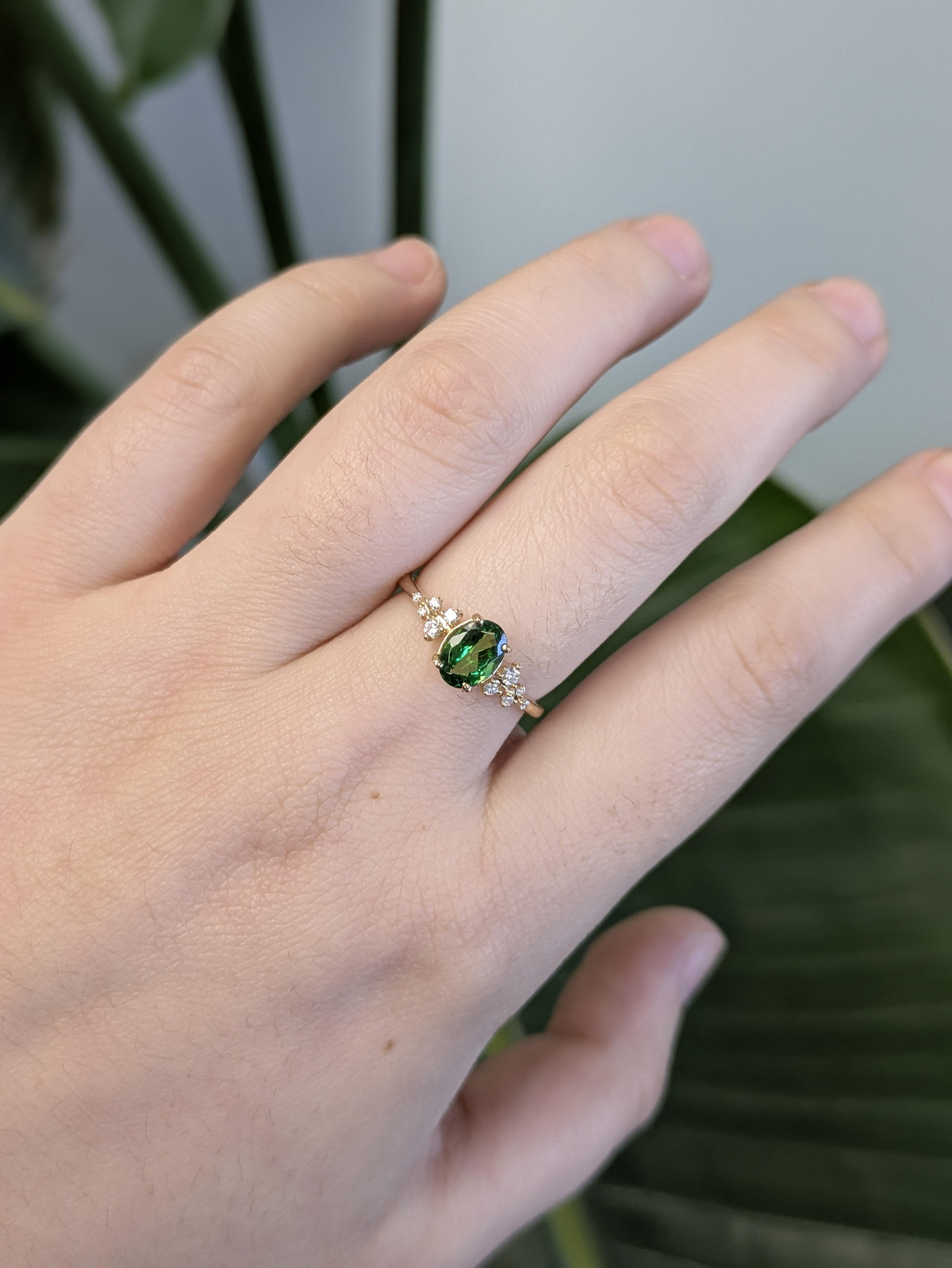 Questo elegante anello in oro giallo 14K presenta al centro un granato tsavorite dal taglio ovale, accentuato da scintillanti diamanti naturali lungo un grazioso gambo passante. La gemma verde brillante e la montatura in oro caldo creano un tocco