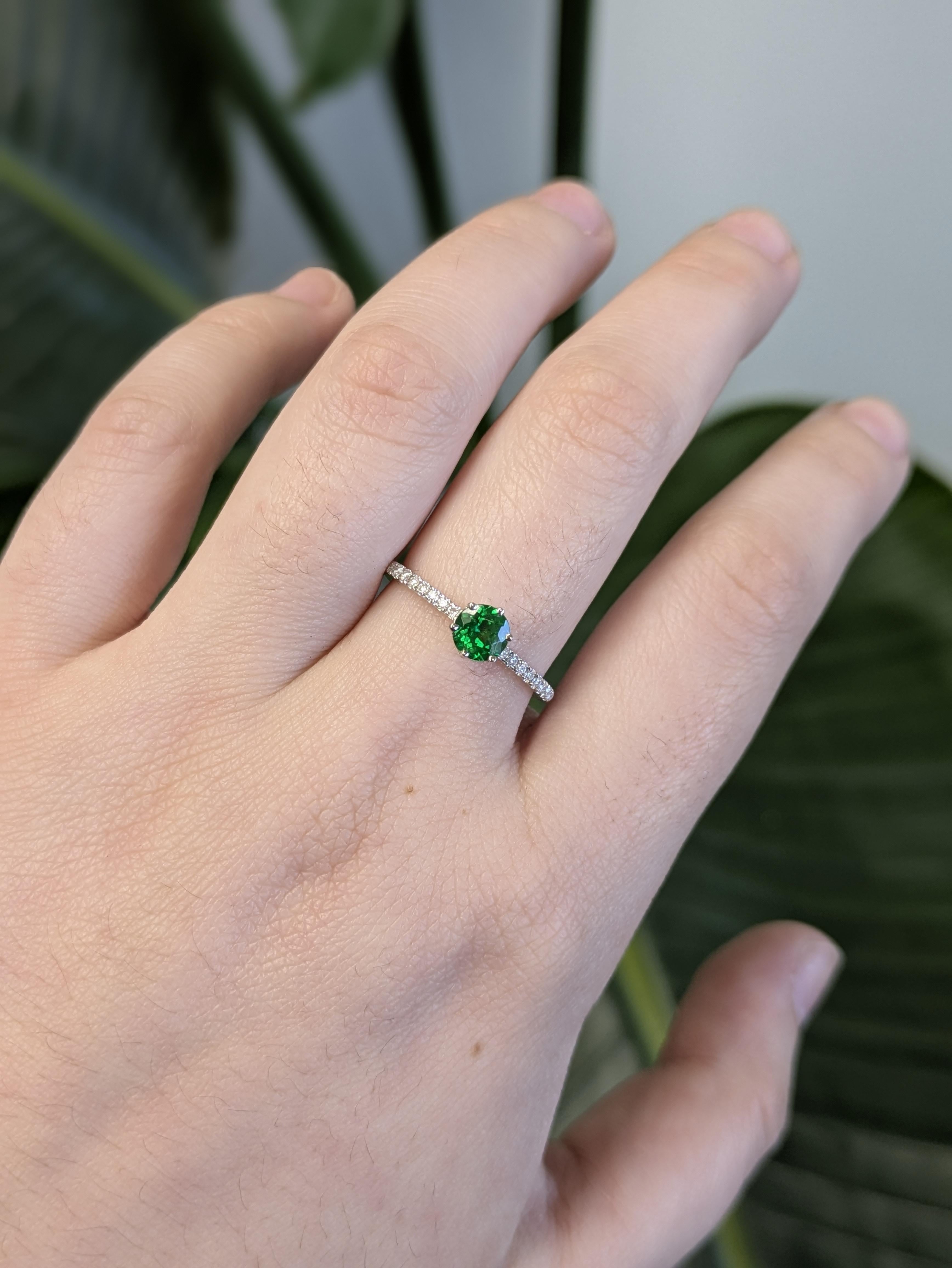 Cette magnifique bague en or blanc 14 carats présente en son centre un brillant grenat tsavorite rond, rehaussé de diamants naturels étincelants. La teinte vert vif de la tsavorite contraste magnifiquement avec l'or blanc élégant, créant un look à
