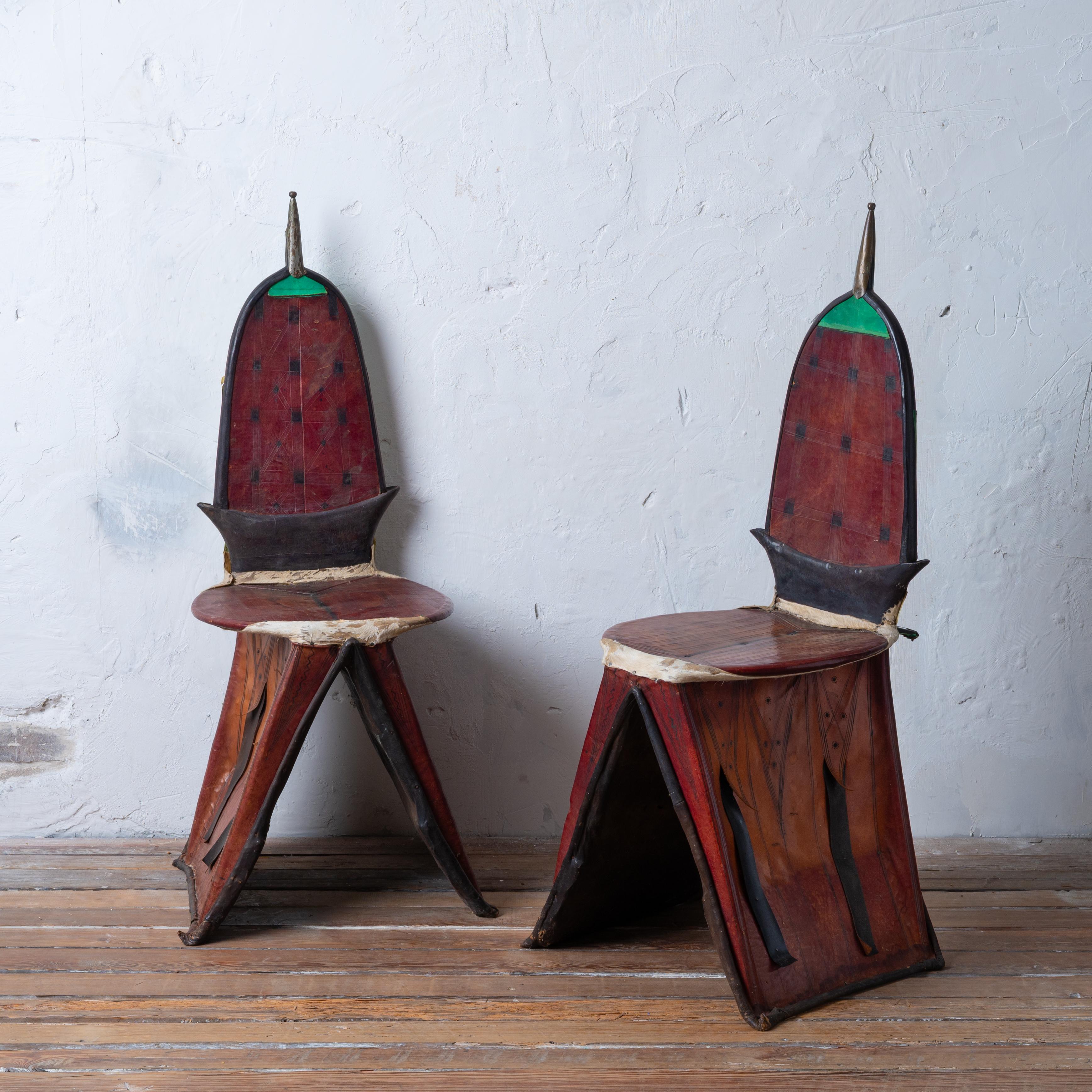 A pair of Tuareg Berber Tamzak camel saddle chairs, Niger Africa, early 20th century.

These saddle chairs are built of sturdy hardwood frames wrapped with various hides and leathers with tooling and dyes and cut metal.

18 ½ inches wide by 18