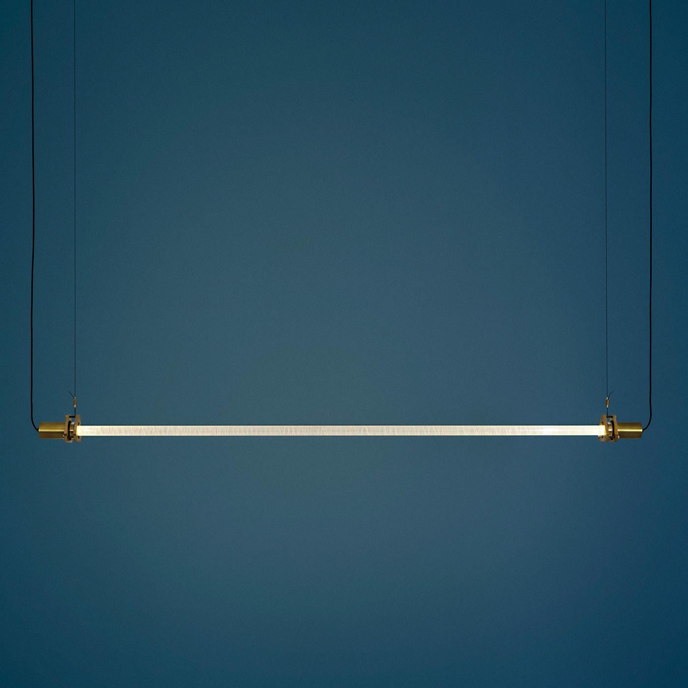 This striking suspension light exudes Industrial allure, serving as an object of strong visual impact in a modern home. A 2 meter-long borosilicate cylinder hides a curved PMMA rod wrapped in cellophane which captures, traps, and refracts a warm