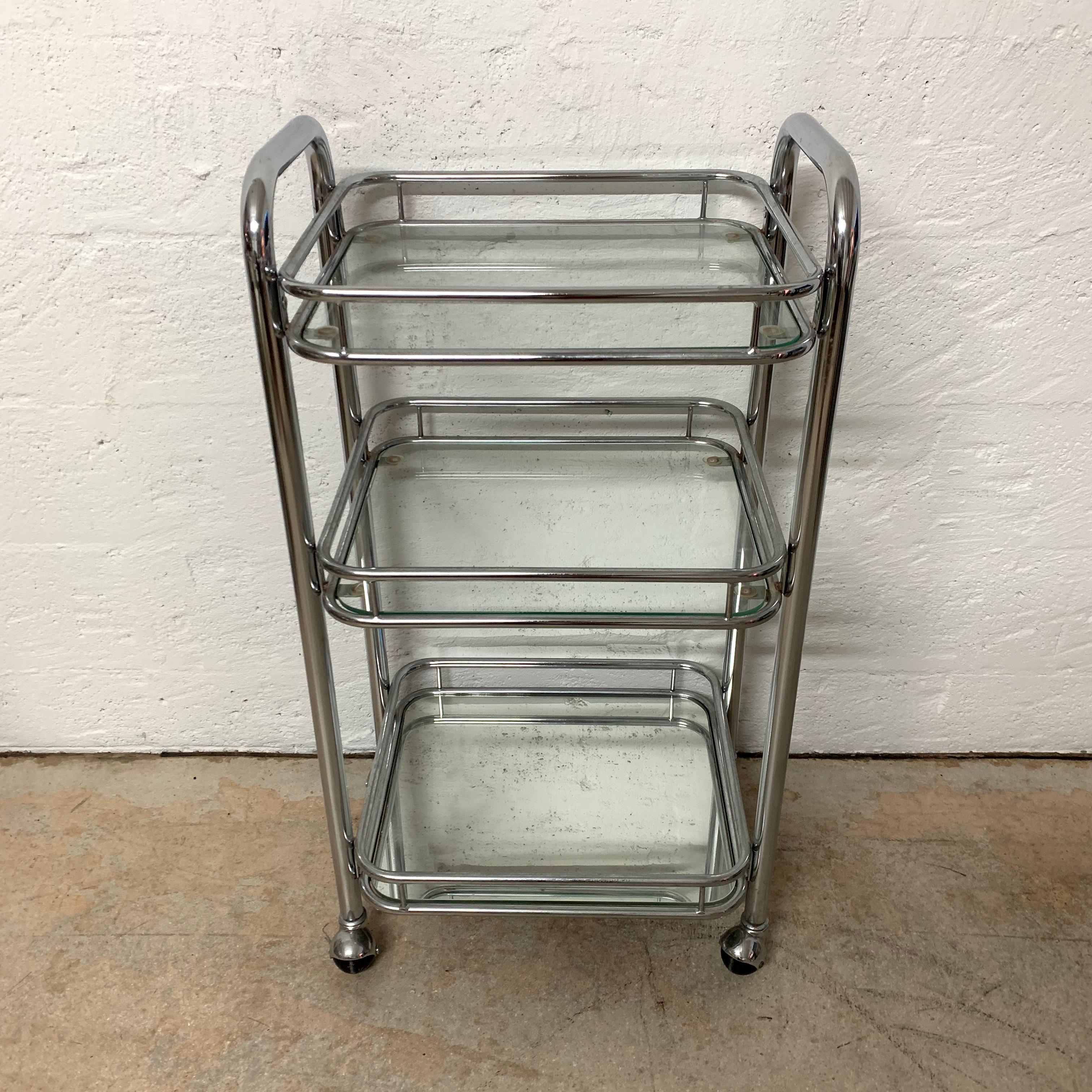 Art Deco style bar cart or trolley rendered in chrome-plated tubular steel with 4 wheels or castors for mobility and 2 glass shelves and a mirrored bottom shelf.