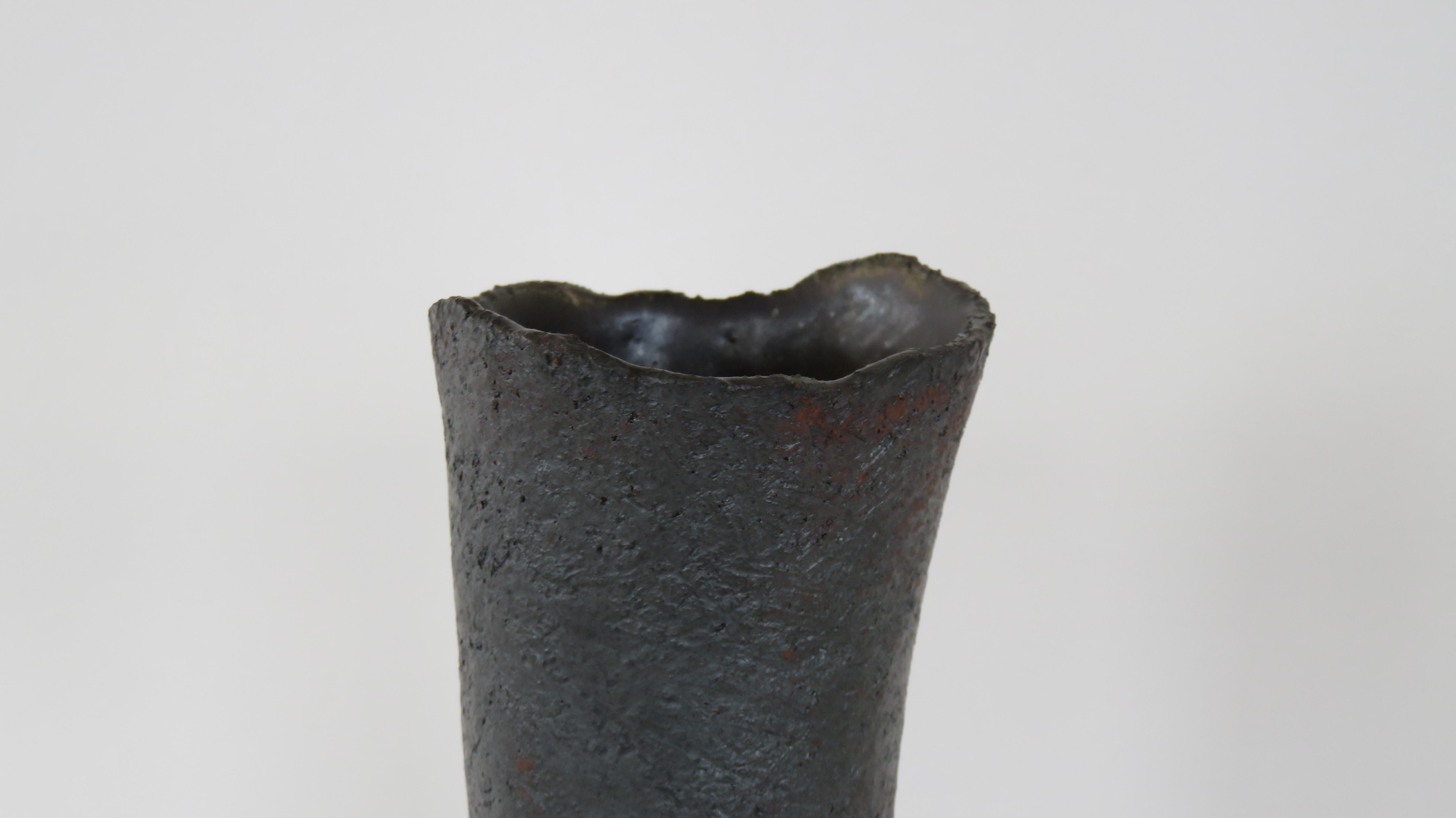 These tall vases in a metallic black glaze over stoneware are weighted on the bottom for tall floral arrangements or branches. Each surface is scraped to show the texture and tone of the clay, with varying bases or knobby edges. The top rims are