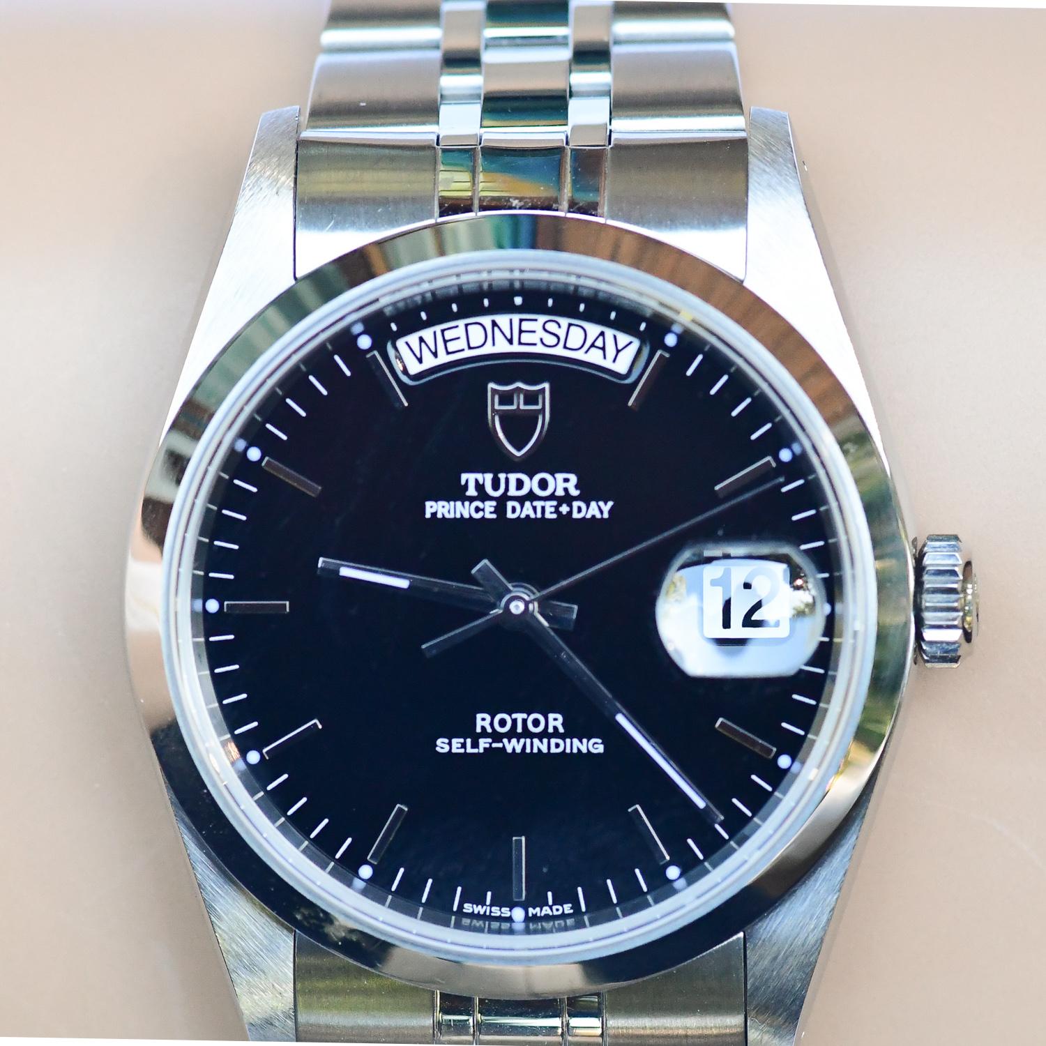 Pre-Owned Tudor Prince Day-Date (76200) self-winding automatic watch, features a 36mm stainless steel case surrounding a black dial on a stainless steel bracelet with folding buckle. Functions include hours, minutes, seconds, day and date. This