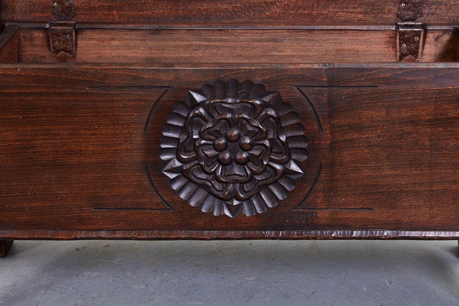 A small coffee table or chest carved with a tudor rose to the front, and having a flat lift top over canted sides with integral arch feet. The whole constructed in the traditional manner, Norfolk school, with dovetail joints and heavy wrought iron