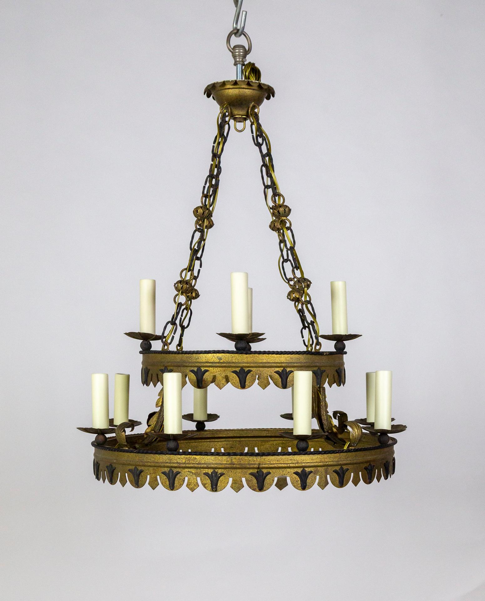 A Mid-Century, Tudor Style, tole chandelier.  It has a double ring structure- with 4 lights on the top and 8 on the bottom- hanging from a unique, decorative chain and painted in matte black and antique brass tones. 30