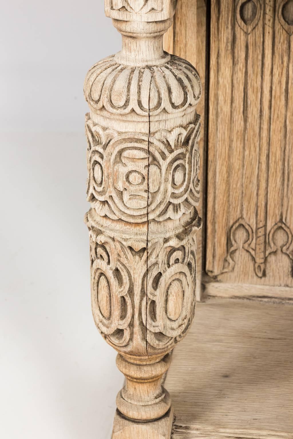 Bleached oak cupboard in the Tudor style with a three door, sloped front. Inside features two adjustable shelves and one long drawer. The exterior features shallow relief carvings of the Tudor rose on a carved skirt with bulb turned legs, circa 1900.