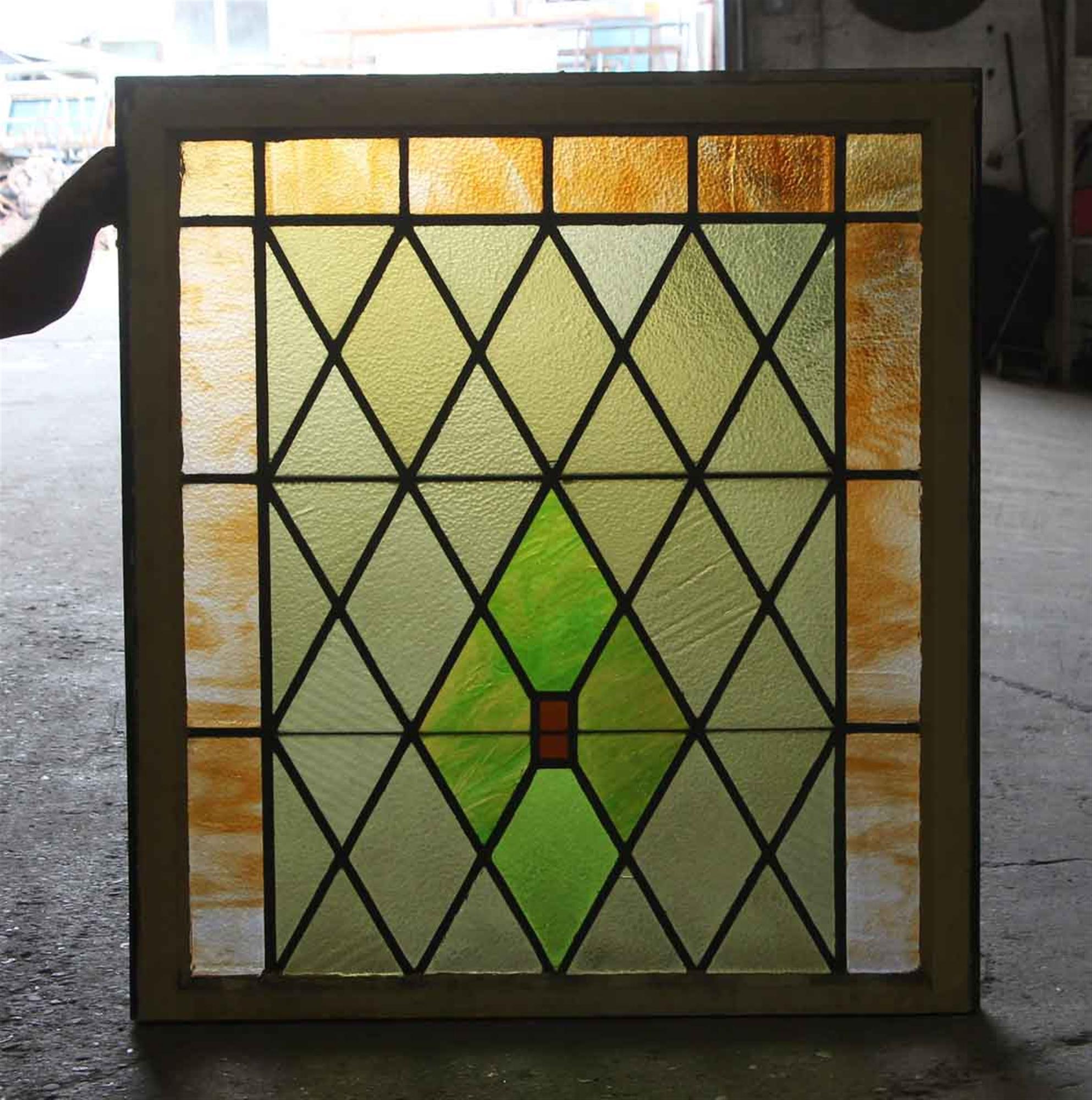 Wood frame top sash stained glass window with diamond patterns typical of the Tudor style. The glass is made up of orange and green colors in varying intensities. The frame is brown on one side and beige on the other. Made circa 1915 during the Arts