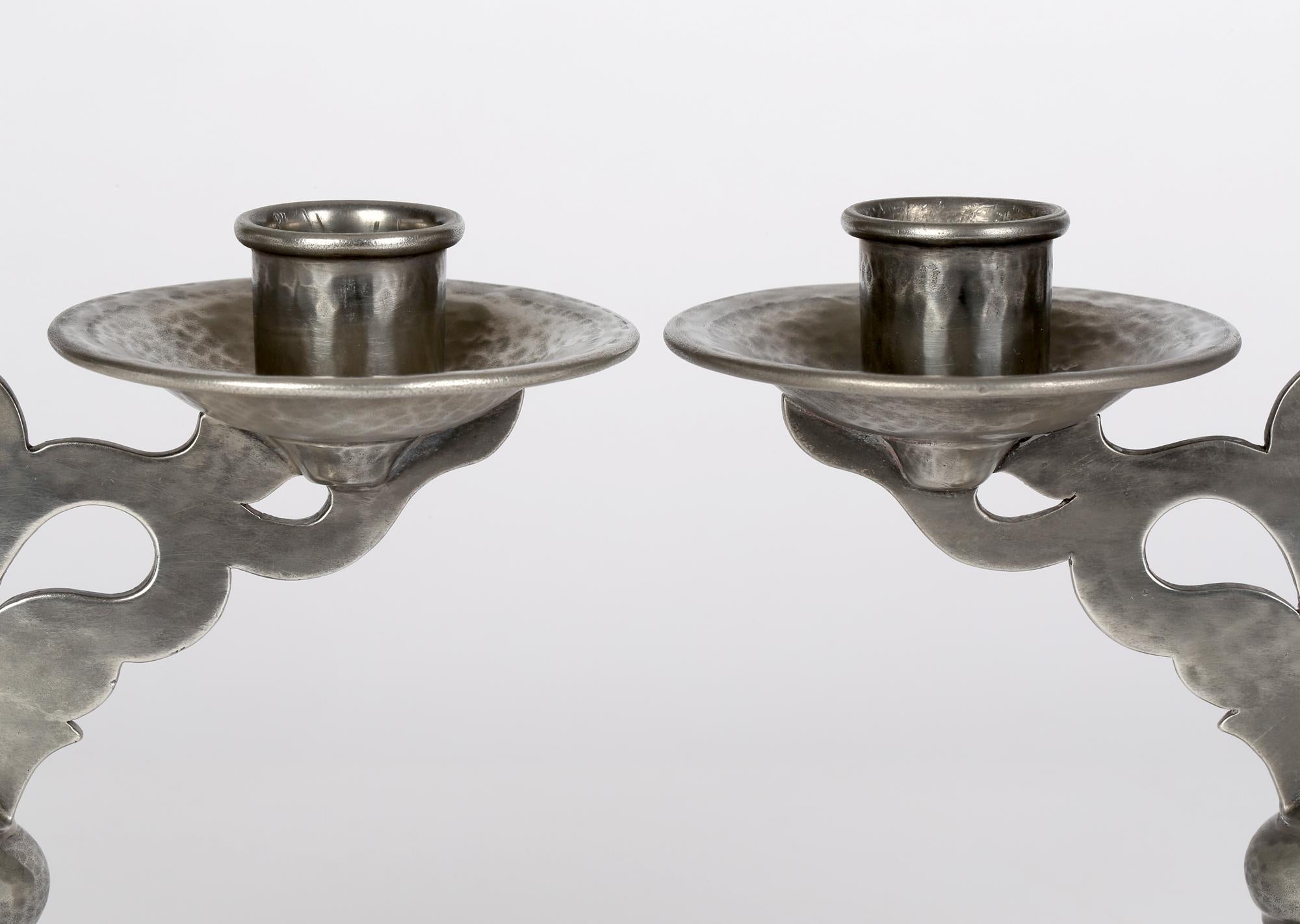 A stylish and fine pair Tudric pewter Arts & Crafts planished double candlesticks dating from around 1920. The candlesticks stand on a wide stepped rounded base rising to the narrow knop stem with a central flat pierced scroll design arm supporting