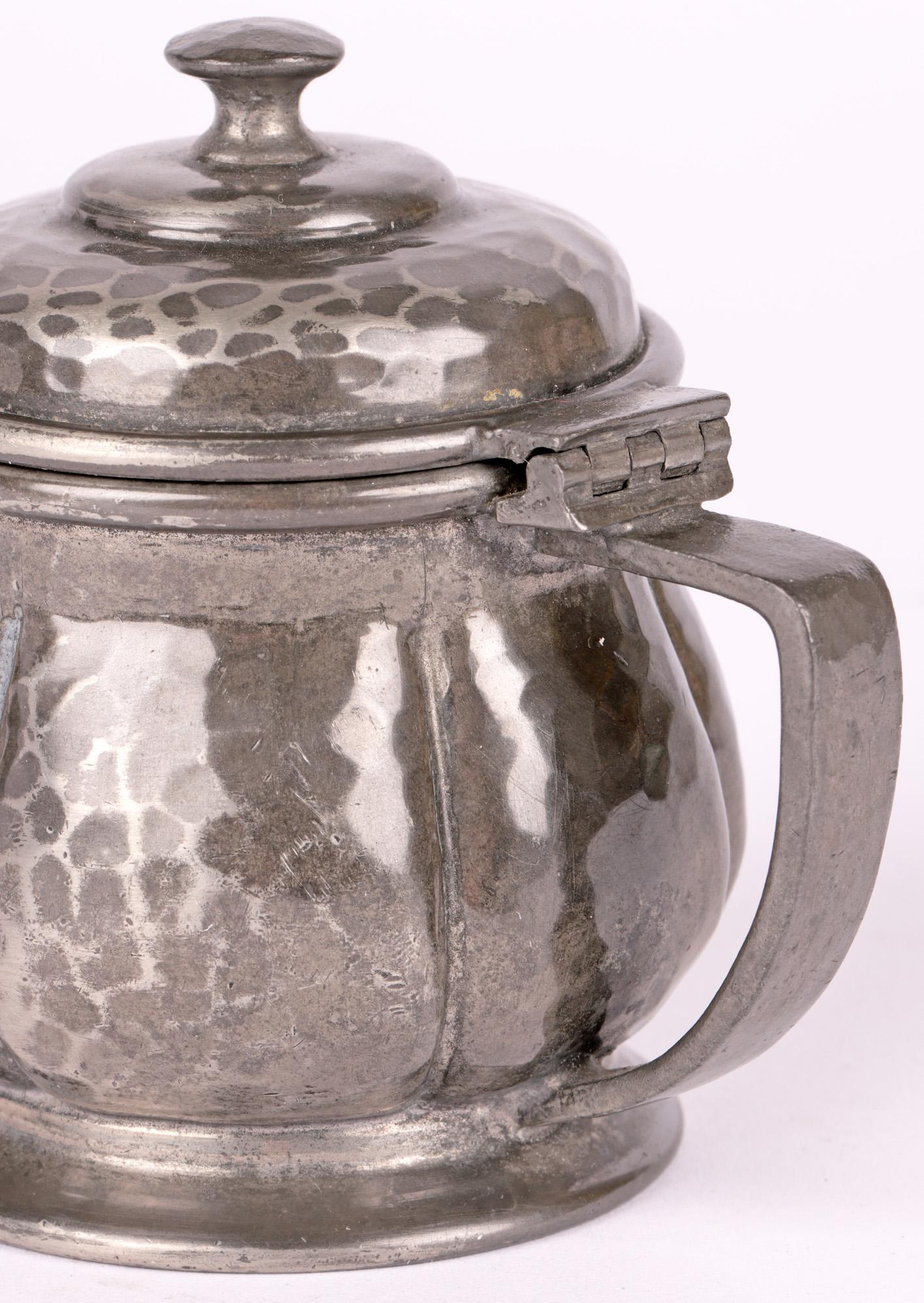 A very fine Arts & Crafts English pewter mustard pot with original glass liner made for Liberty & Co by Tudric and dating from the early 20th century. The mustard pot stands raised on a wide skirted foot and has a round gourd shaped body with flat