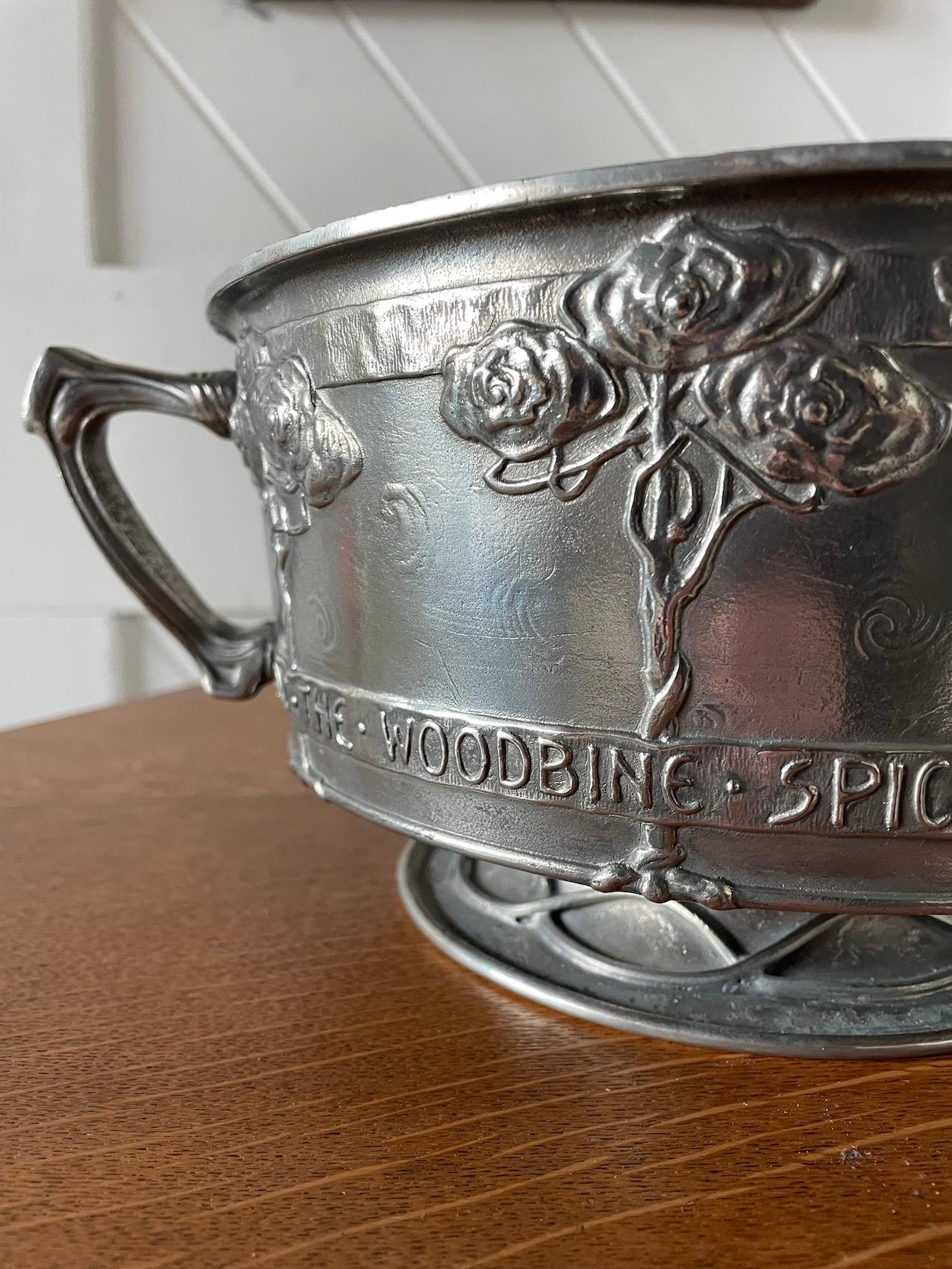 Arts & Crafts twin handle ‘Tudric’ pewter rose bowl 

With stylised rose tree design and motto:

“And The Woodbine Spices Are Wafted Abroad And The Musk Of The Rose Is Blown”

From the poem “Come Into The Garden Maud” by Alfred, Lord Tennyson 
