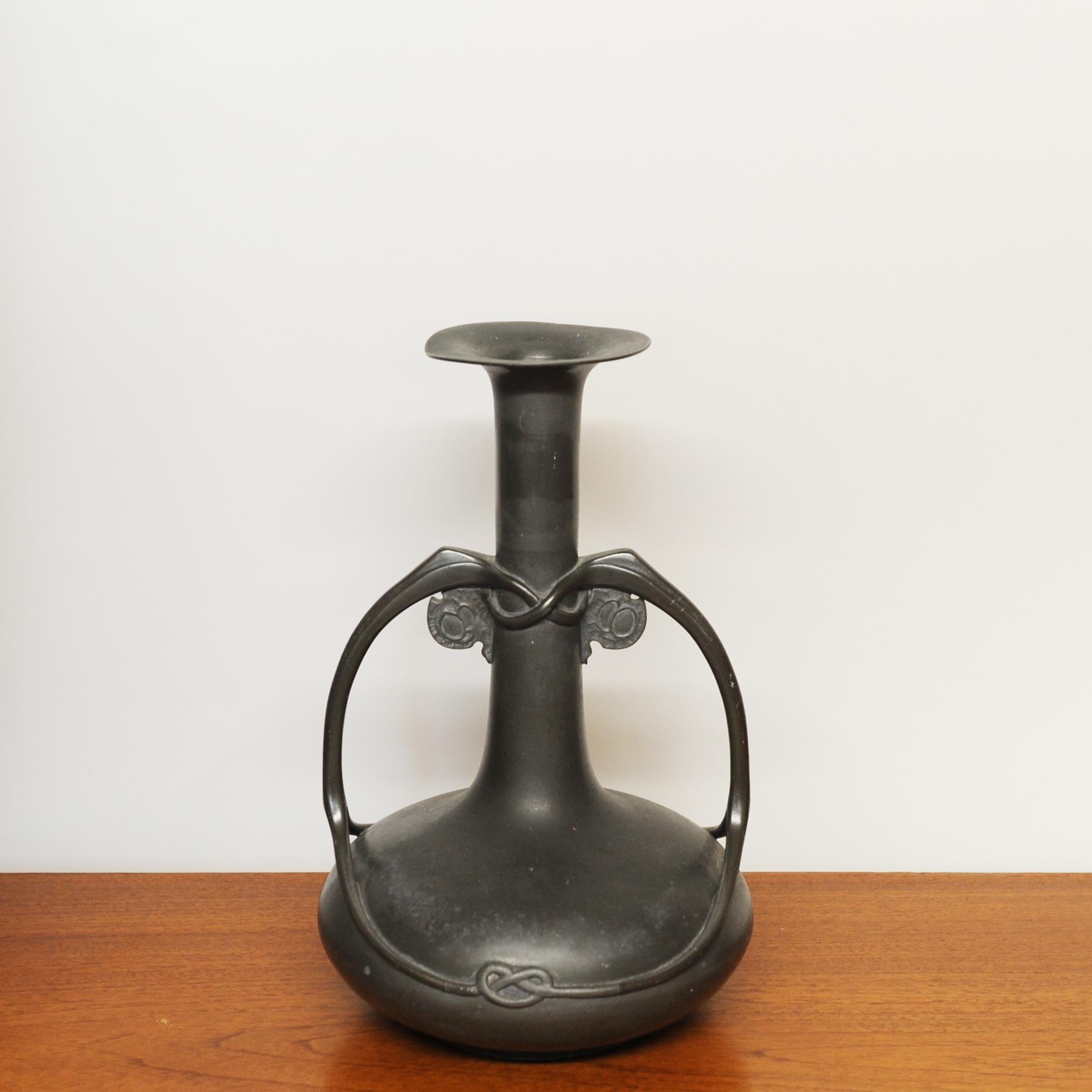 A Tudric pewter twin handled vase with a tall cylindrical neck and everted rim, the handles of sinuous organic form fashioned with Celtic entrelac motifs.

Stamped - TUDRIC 0214

Designer - Archibald Knox

Design Period - 1900 to 1909

Style - Art