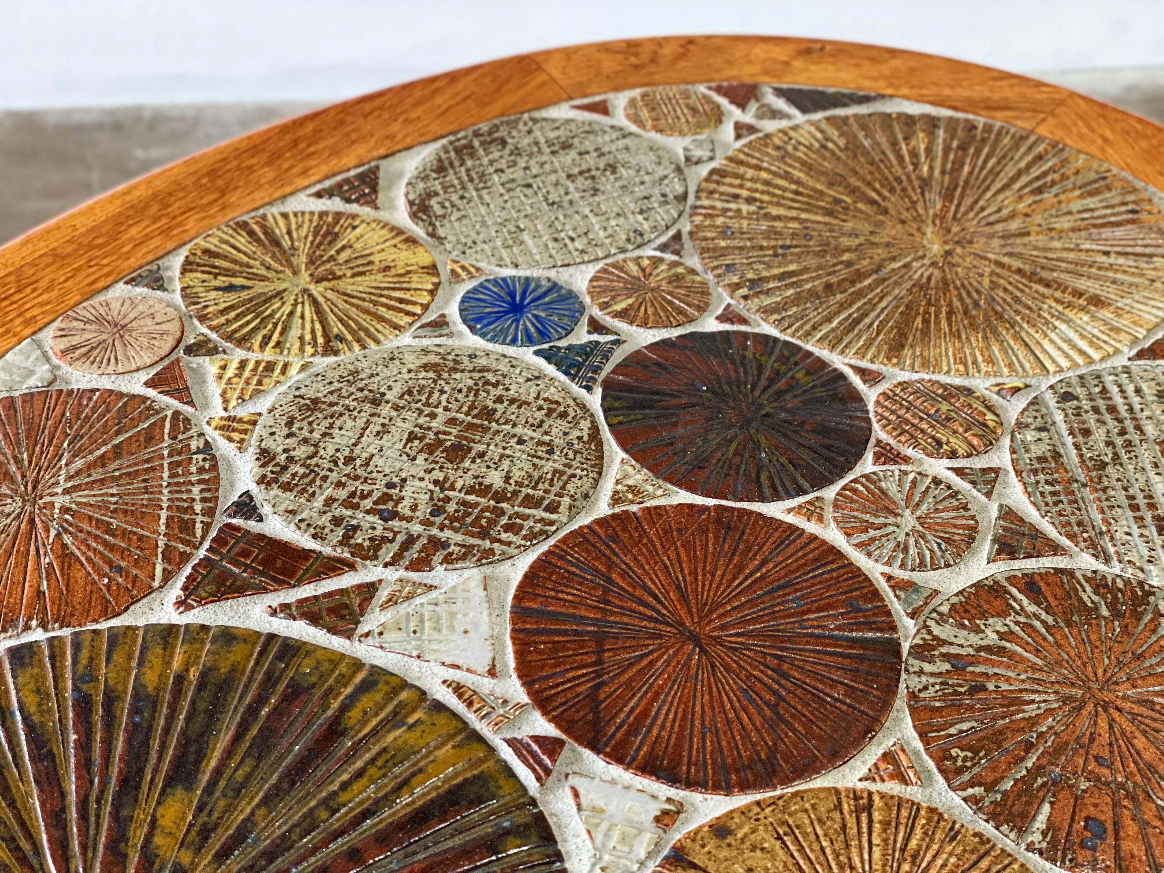 Danish modern side or end table by Tue Poulsen for Haslev Møbelsnedkeri A/S, Denmark. Oval form top with Solid turned teak legs. Top is inset with incised, hand painted bright glazed ceramic tiles in shades of blue, brown, maroon, mustard, cream,