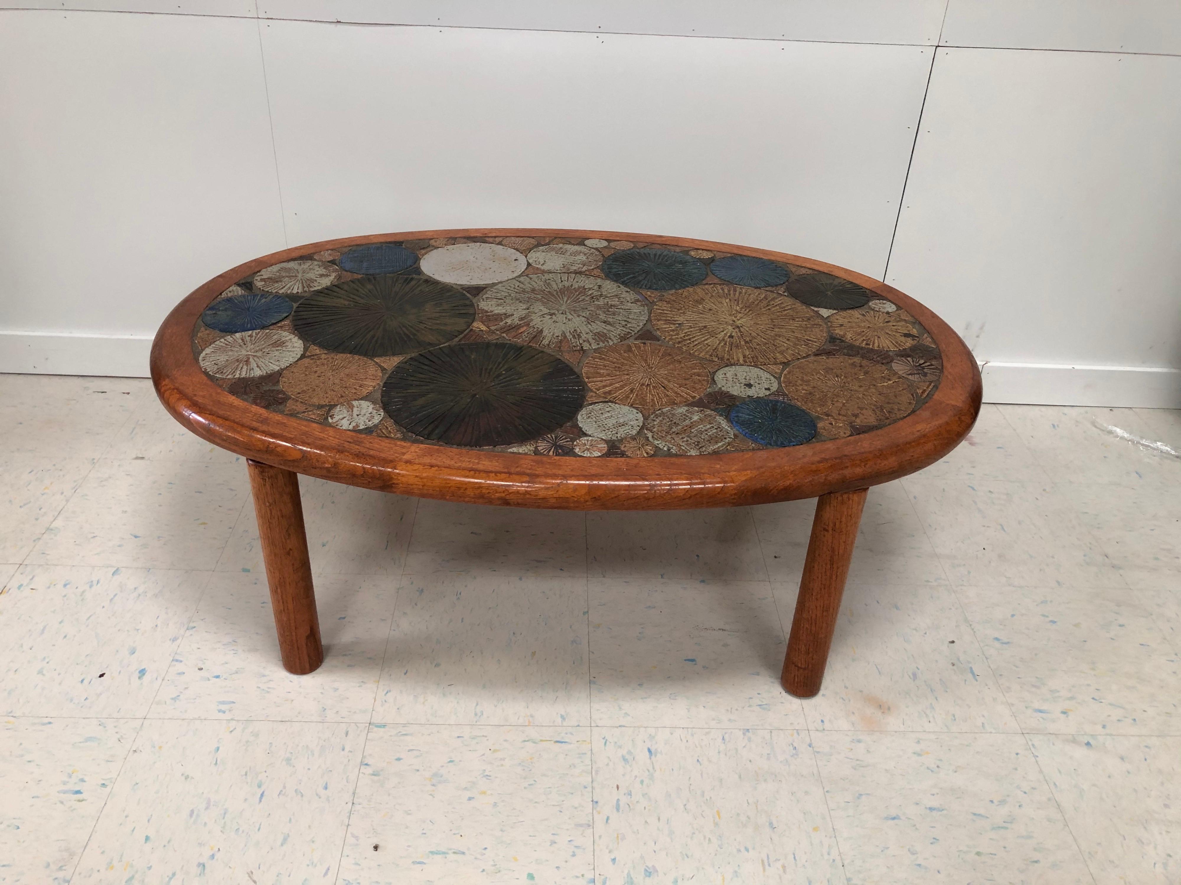 Danish modern handcrafted Tue Poulsen coffee cocktail table for Haslev Møbelsnedkeri A/S, Denmark. Featuring an oval teak form, inset with incised, hand painted bright glazed ceramic wheels in blue, brown, maroon, mustard, cream, rust and brown.