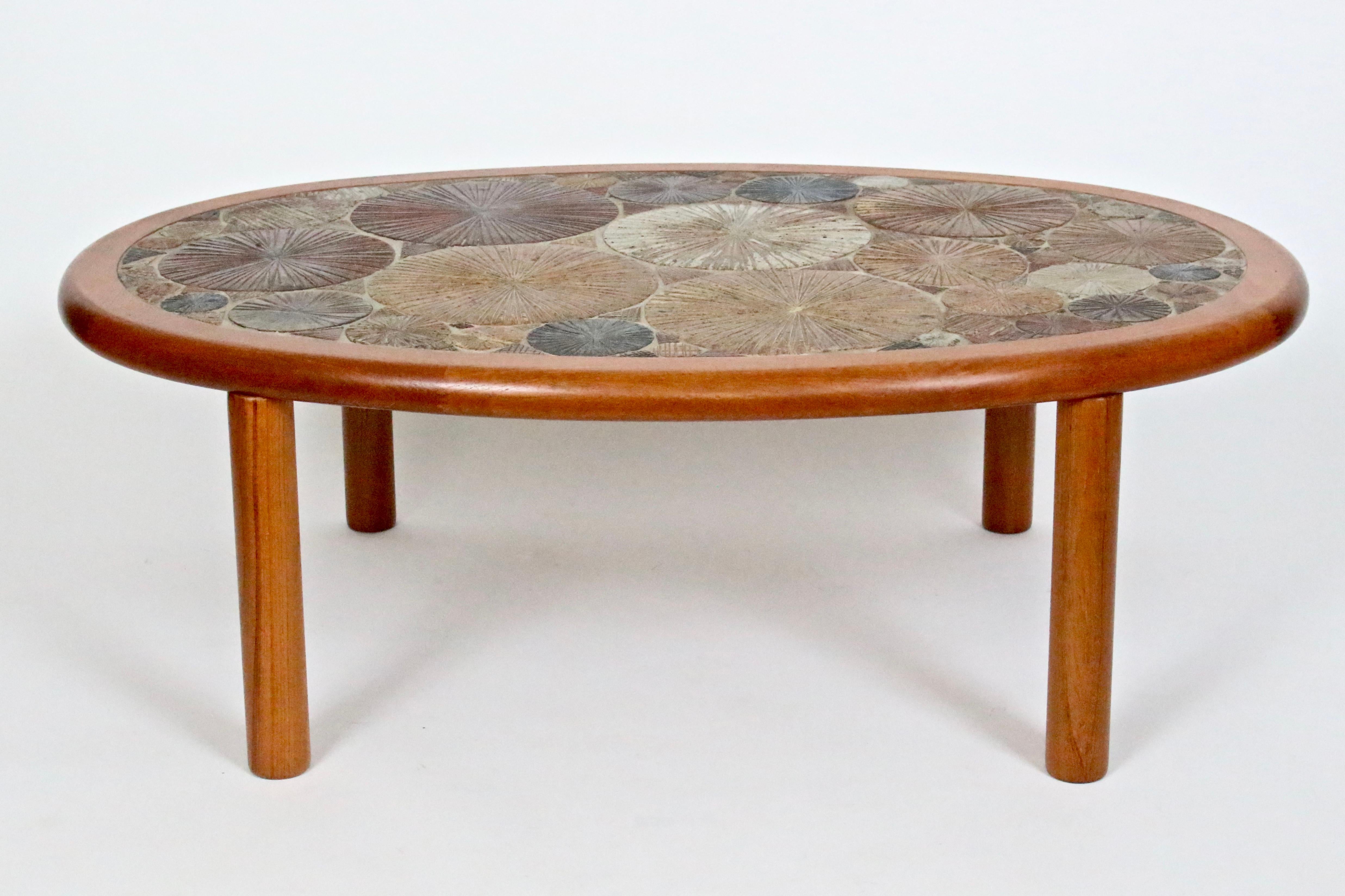 Danish modern handcrafted Tue Poulsen coffee cocktail table for Haslev Møbelsnedkeri A/S, Denmark. Featuring an oval teak form, inset with incised, hand painted bright glazed ceramic wheels in blue, brown, maroon, mustard, cream, rust and brown.