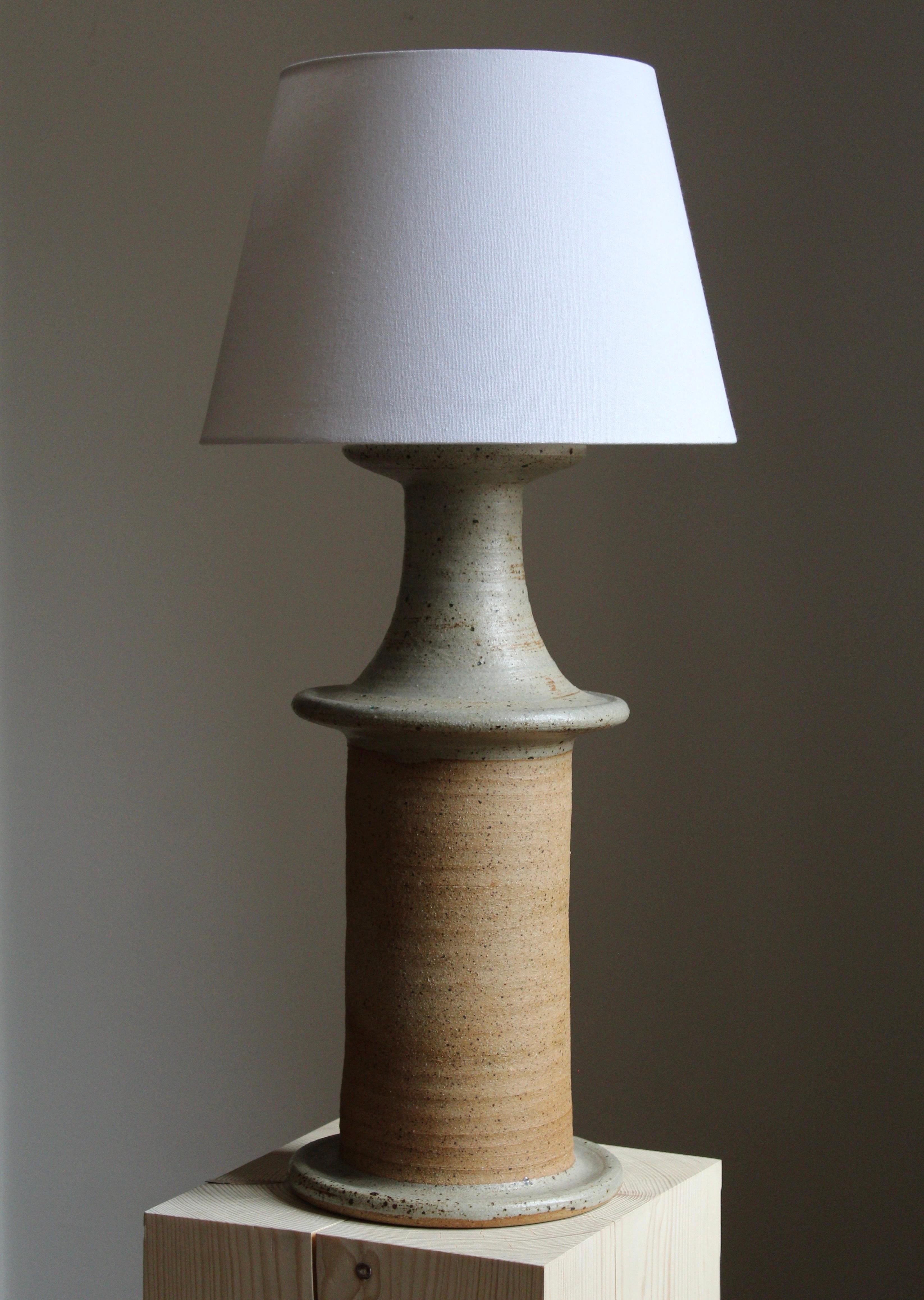 A large and sculptural table lamp. Produced and designed by Tue Poulsen, Denmark, 1960s. The underside of the base stamped.

In grey / beige stoneware. 

Sold without lampshade. Stated dimensions exclude lampshade.

Other designers of the