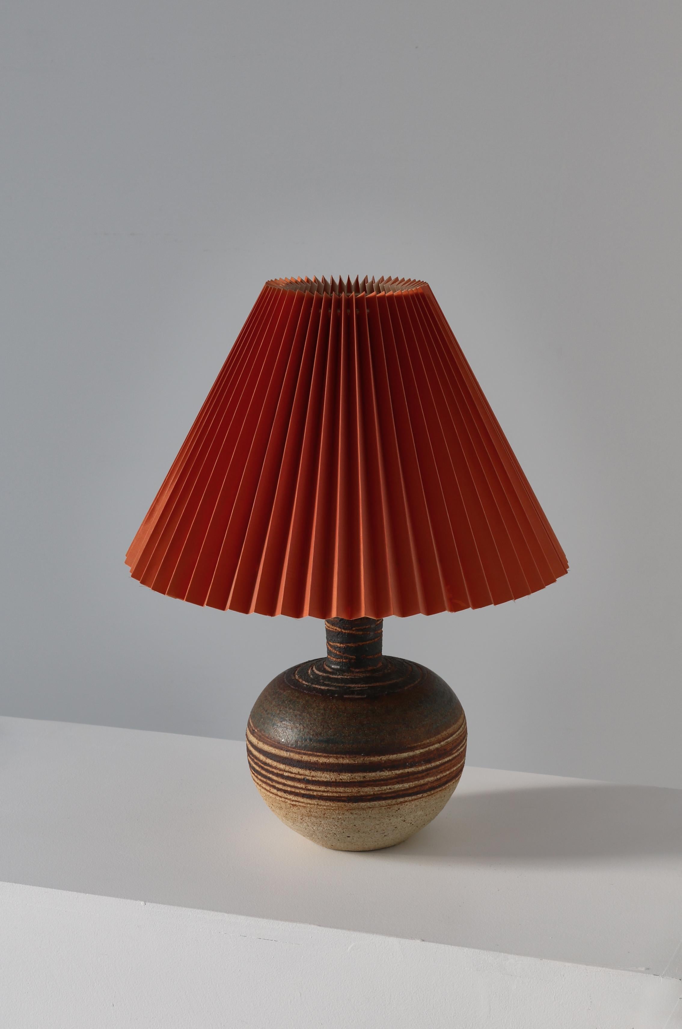Wonderful 1960s design by Danish ceramics artist Tue Poulsen. Handcrafted table lamp in chamotte stoneware with glazing in earth colors. Great condition. Original burned red shade. Marked with 