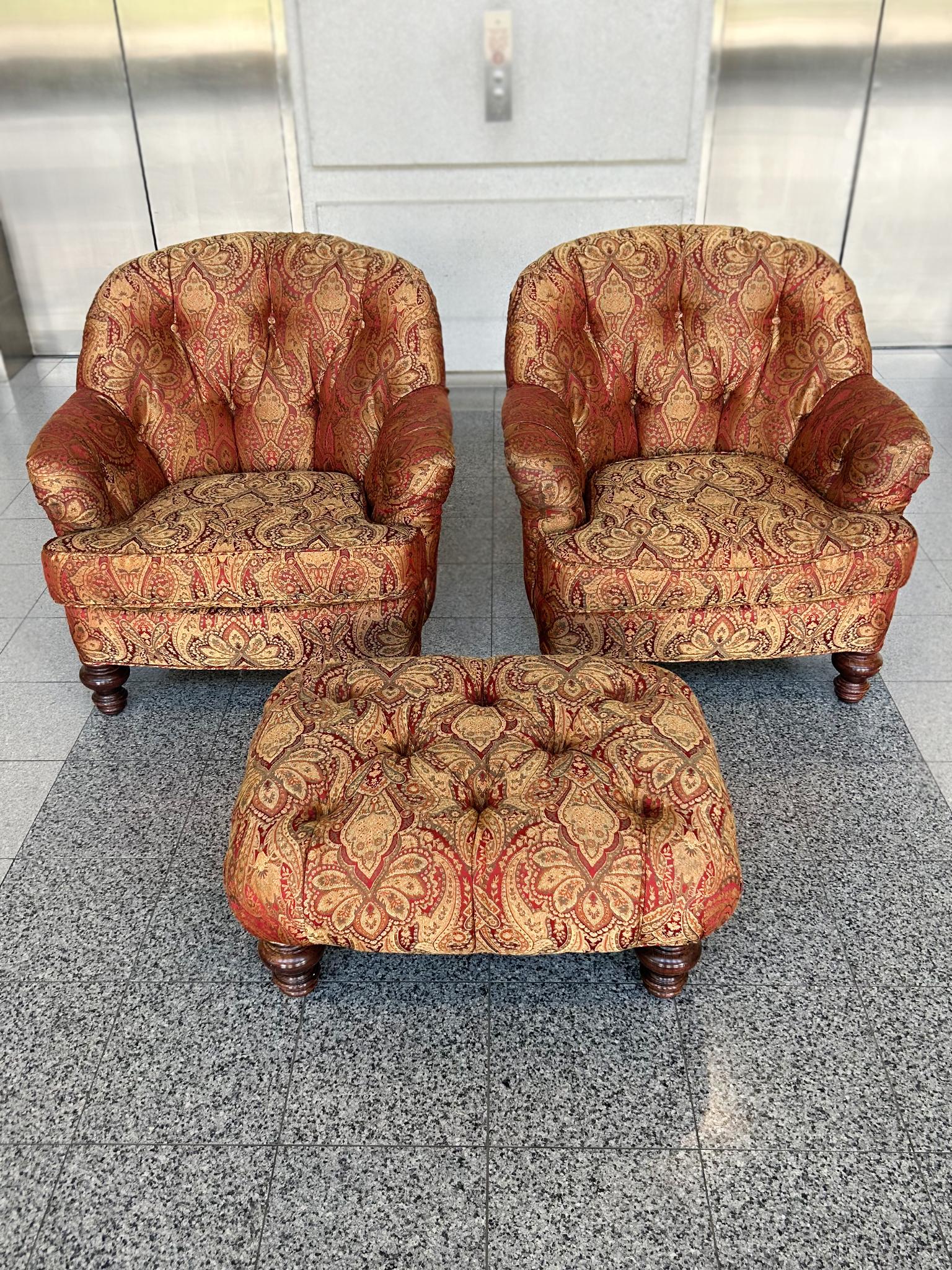 This vintage set consists of two tufted armchairs and one ottoman, crafted in the traditional style of George Smith. Each piece is upholstered in a paisley-patterned weave with a palette of mainly reds, pinks, and cream. The front wood legs of the