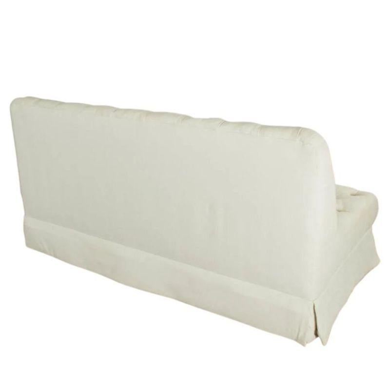 A vintage, armless, tufted, white cotton, three seat sofa from a Daniel Romualdez designed home. The vintage sofa is American made, of textured white cotton with button tufts to seat and back, with tailored skirt on all sides.