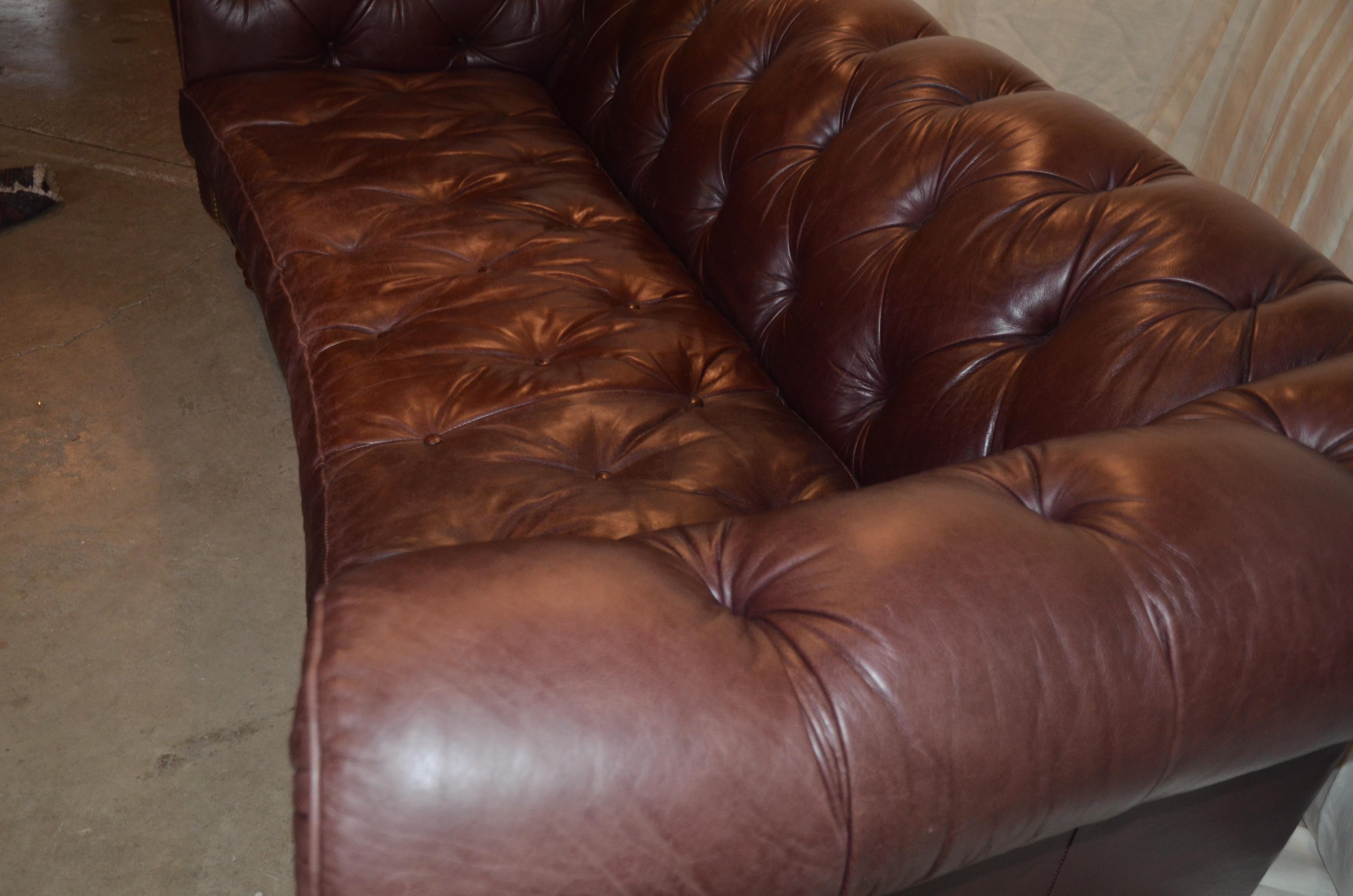 High quality tufted leather sofa by renowned American maker Century Furniture. The sofa has a slight curve to the front with elegant rolled arms, turned wood feet and brass nailhead details. The leather is a beautiful dark brown color with the