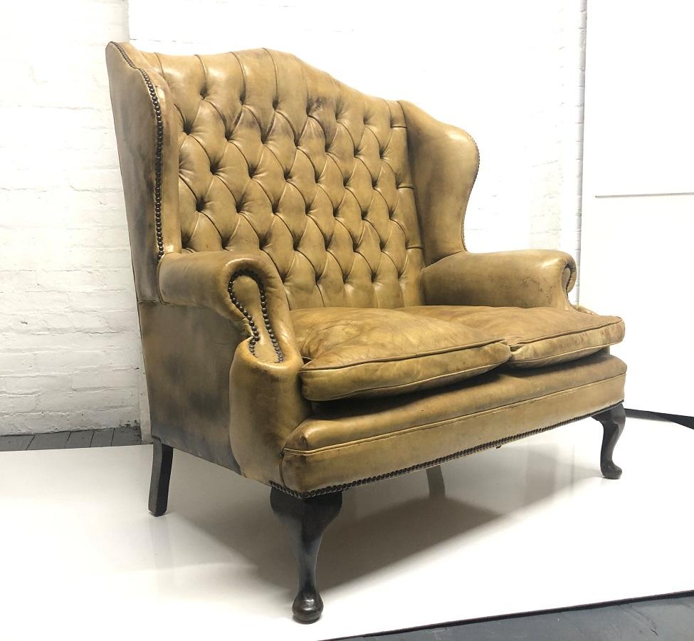 Tufted, original, leather wingback loveseat in the style of Chippendale. Has a high back, wood legs, nice grain and patina to the leather. Nice look for a hallway, study, library or den.  Also, Chesterfield style.