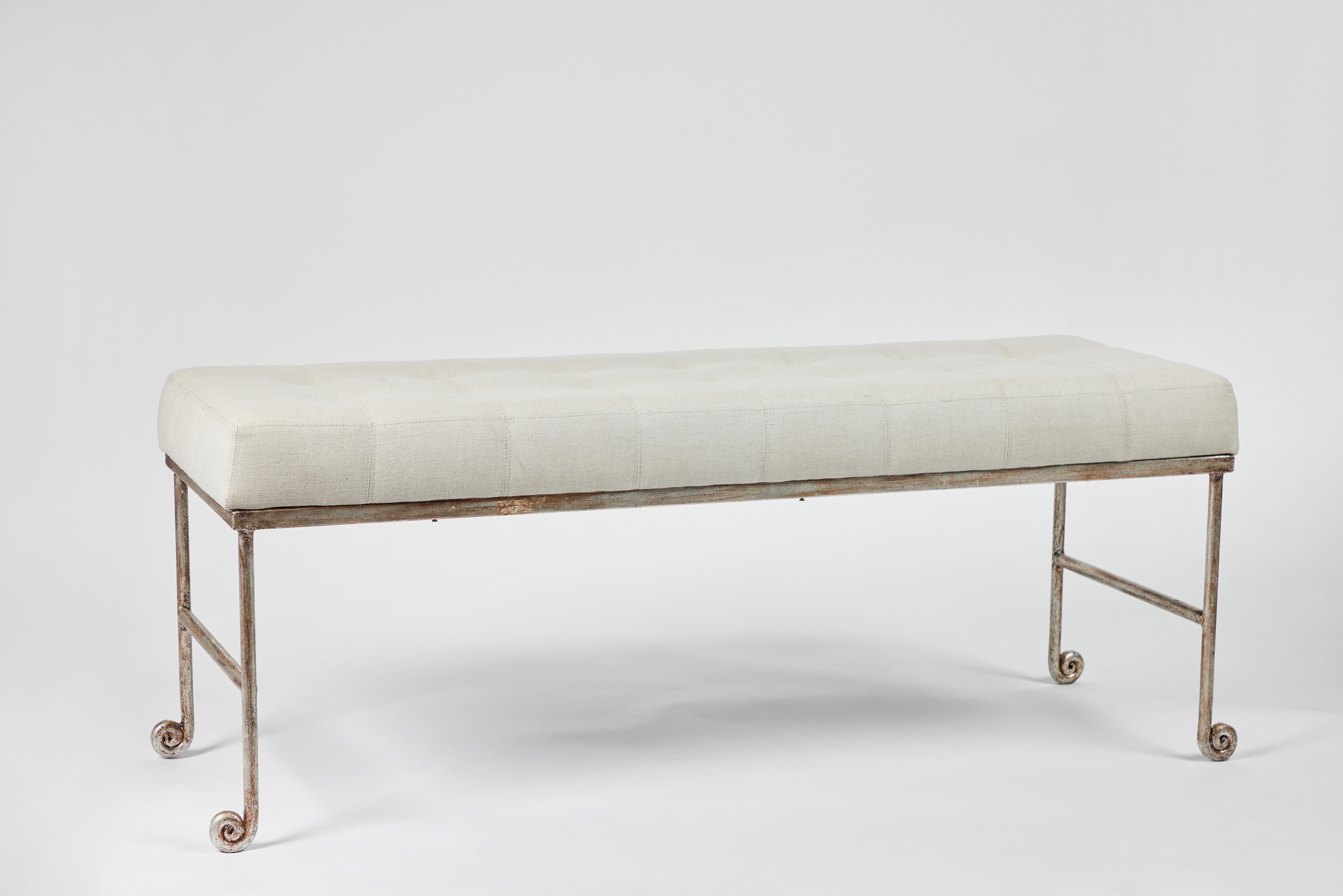 Silvered iron bench with curled feet like a fiddlehead fern. Tufted seat cushion in cream linen. The 